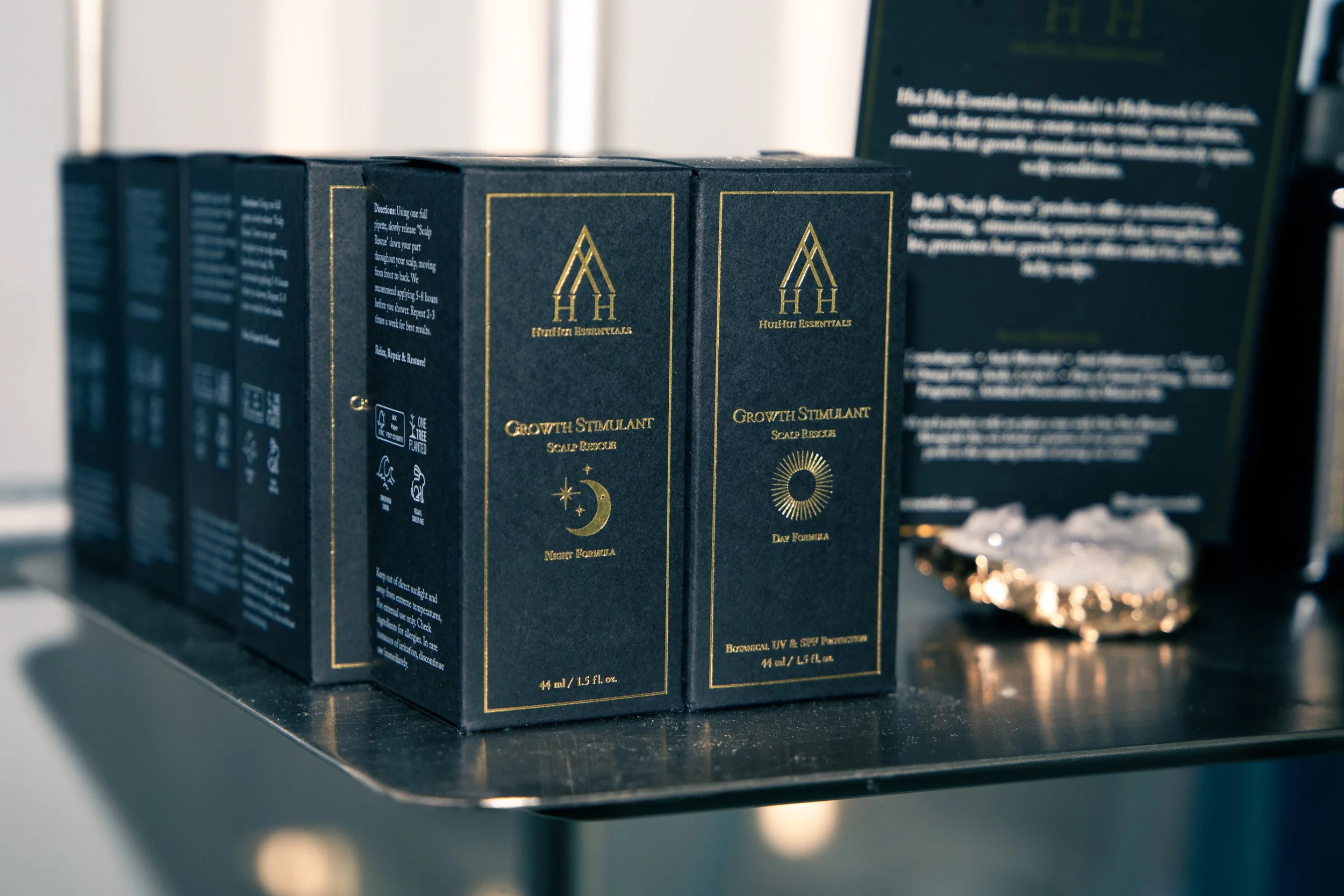 Close-up of skincare product boxes labeled 'Growth Stimulant + Scalp Rescue' from HuiHui Essentials, placed on a black surface with a blurred background.