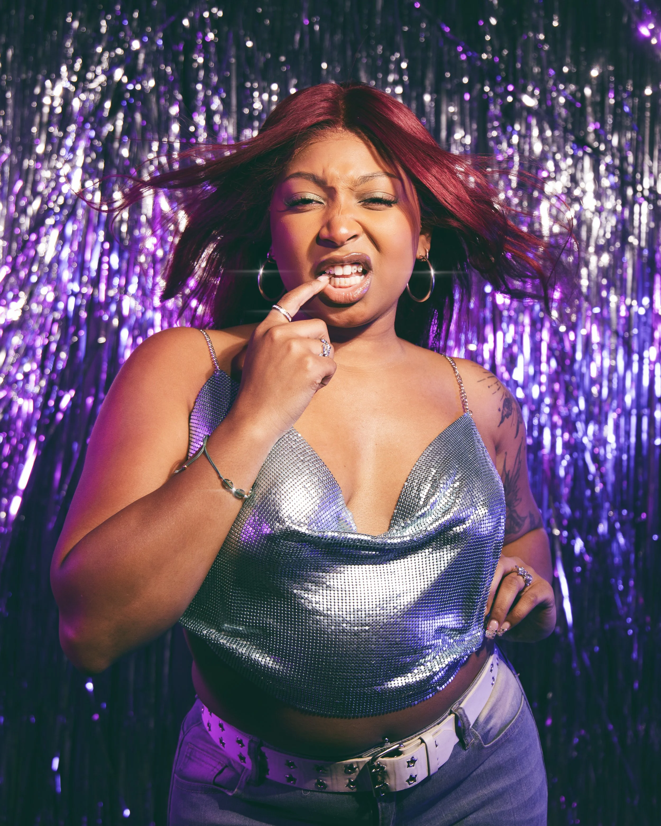 Local Dallas, Texas, DFW Non-traditional Fashion Editorial Creative Portraits Cover Art Photographer Photoshoot. Musician Seihara . A woman with red hair, wearing hoop earrings and a silver sequined top, pulls her lip with her finger, standing in fro
