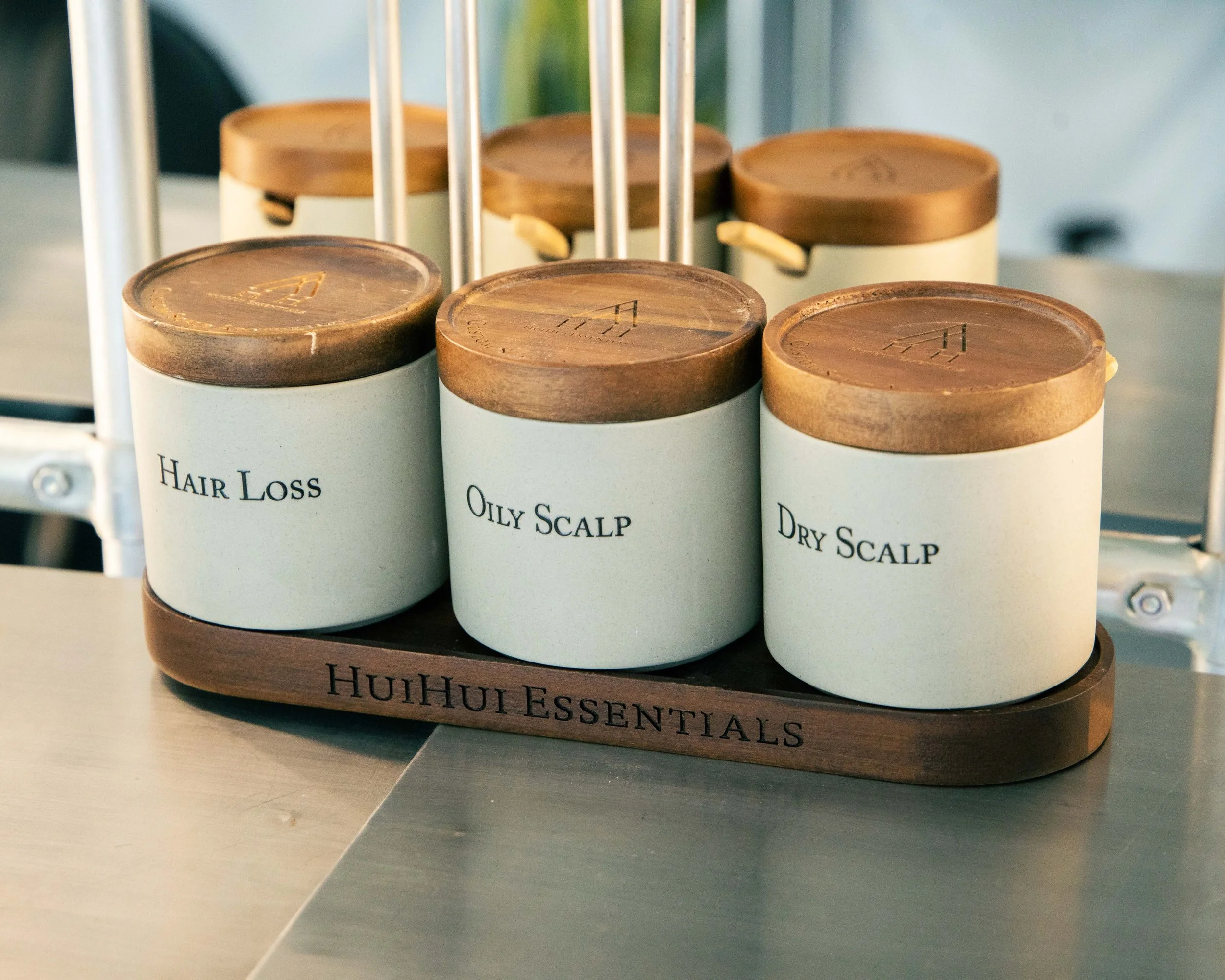 A display of essential oils in jars labeled for hair loss, oily scalp, and dry scalp on a wooden stand labeled 'HuiHui Essentials'.