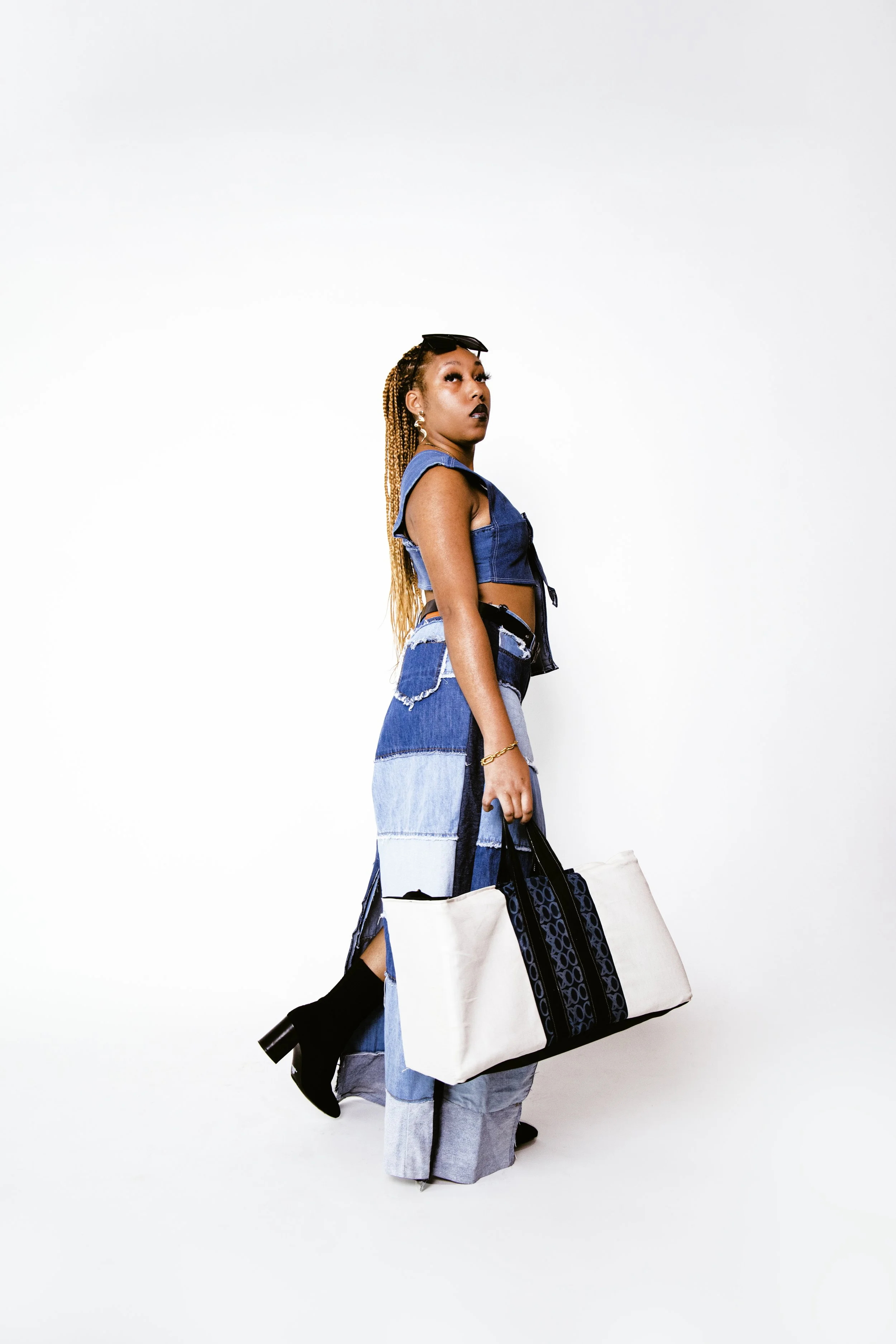 Local Dallas, Texas, DFW Non-traditional Fashion Editorial Creative Portraits Cover Art Photographer Photoshoot. A woman with braided hair and dark lipstick standing against a plain white background, holding a large tote bag, wearing a sleeveless den