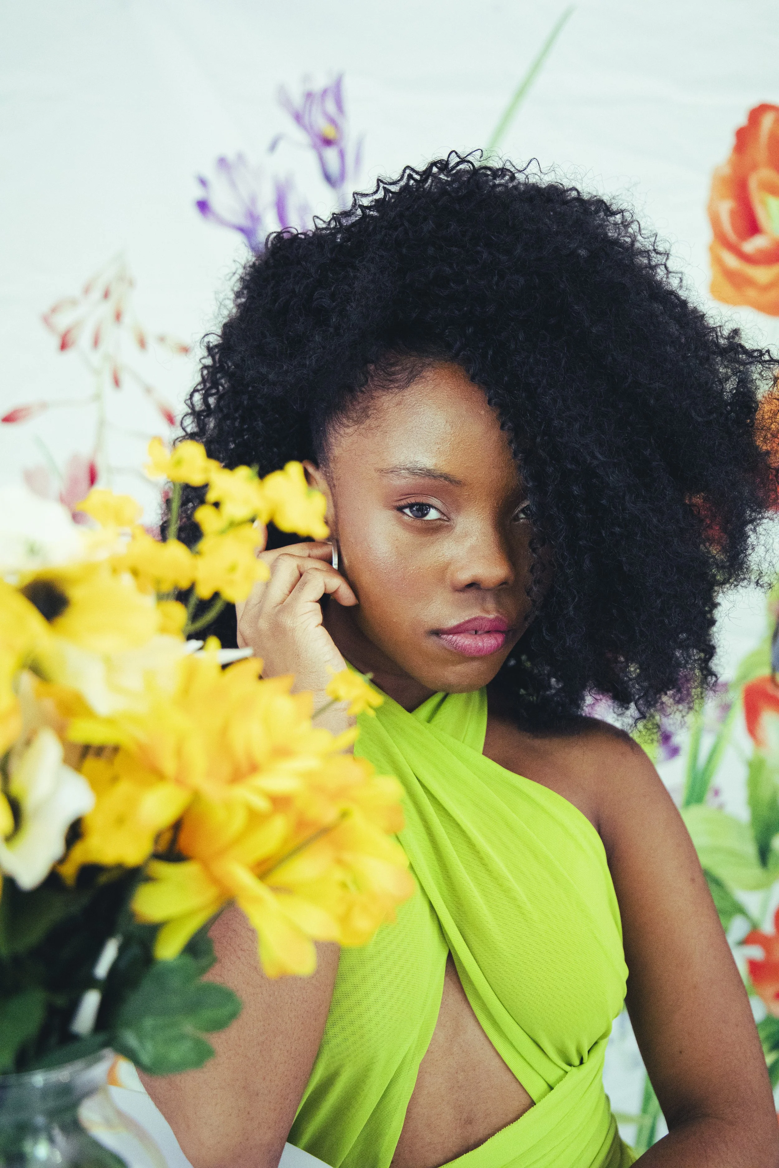 Local Dallas, Texas, DFW Non-traditional Fashion Editorial Creative Portraits Cover Art Photographer Photoshoot. Chanti .A woman with dark, curly hair wearing a bright green dress, surrounded by colorful flowers, with a floral background.