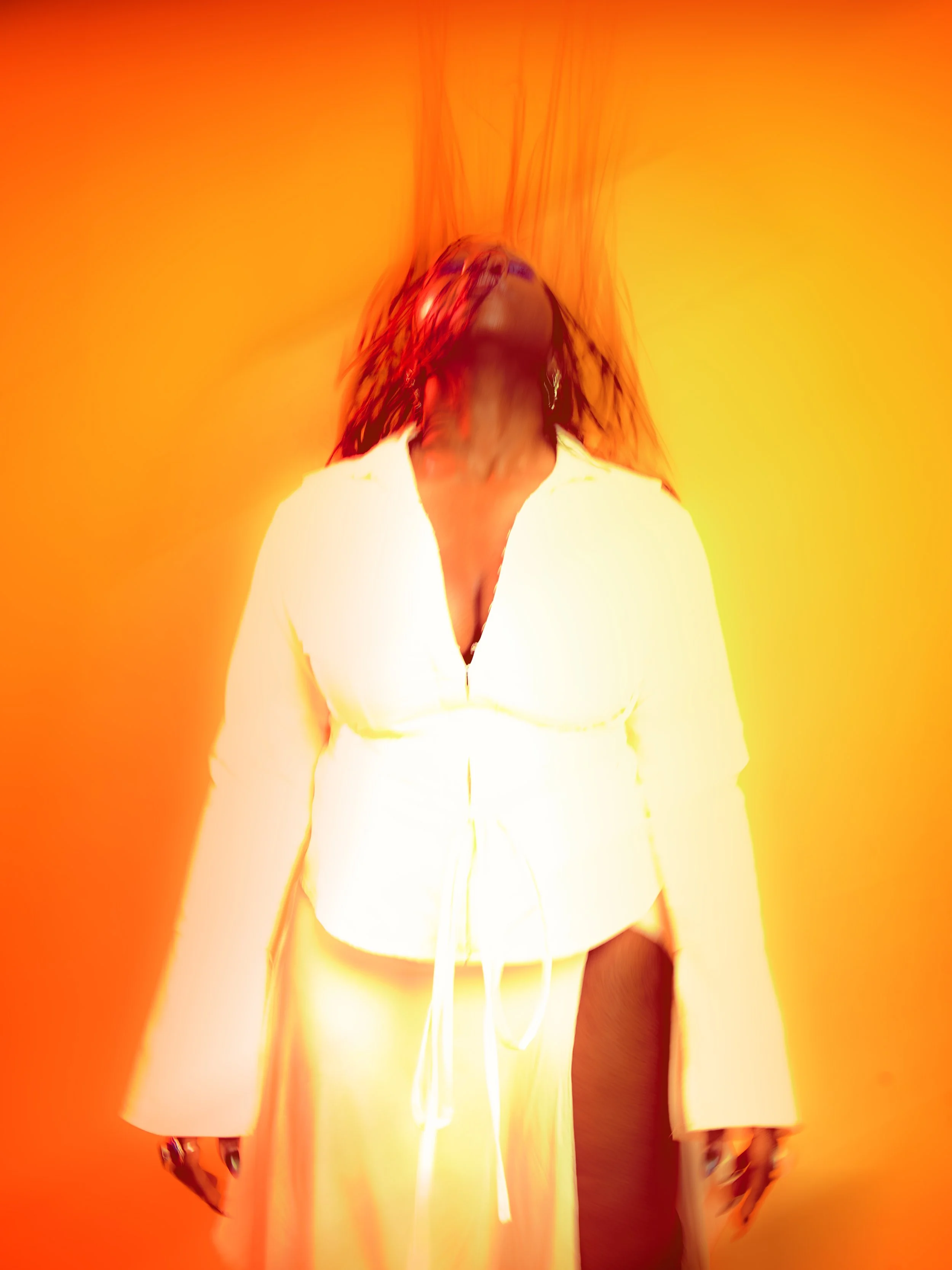 Local Dallas, Texas, DFW Non-traditional Fashion Editorial Creative Portraits Cover Art Photographer Photoshoot. Musician Courtney Noir . Person with dark hair wearing a white shirt standing against an orange and yellow background, with distortion ef