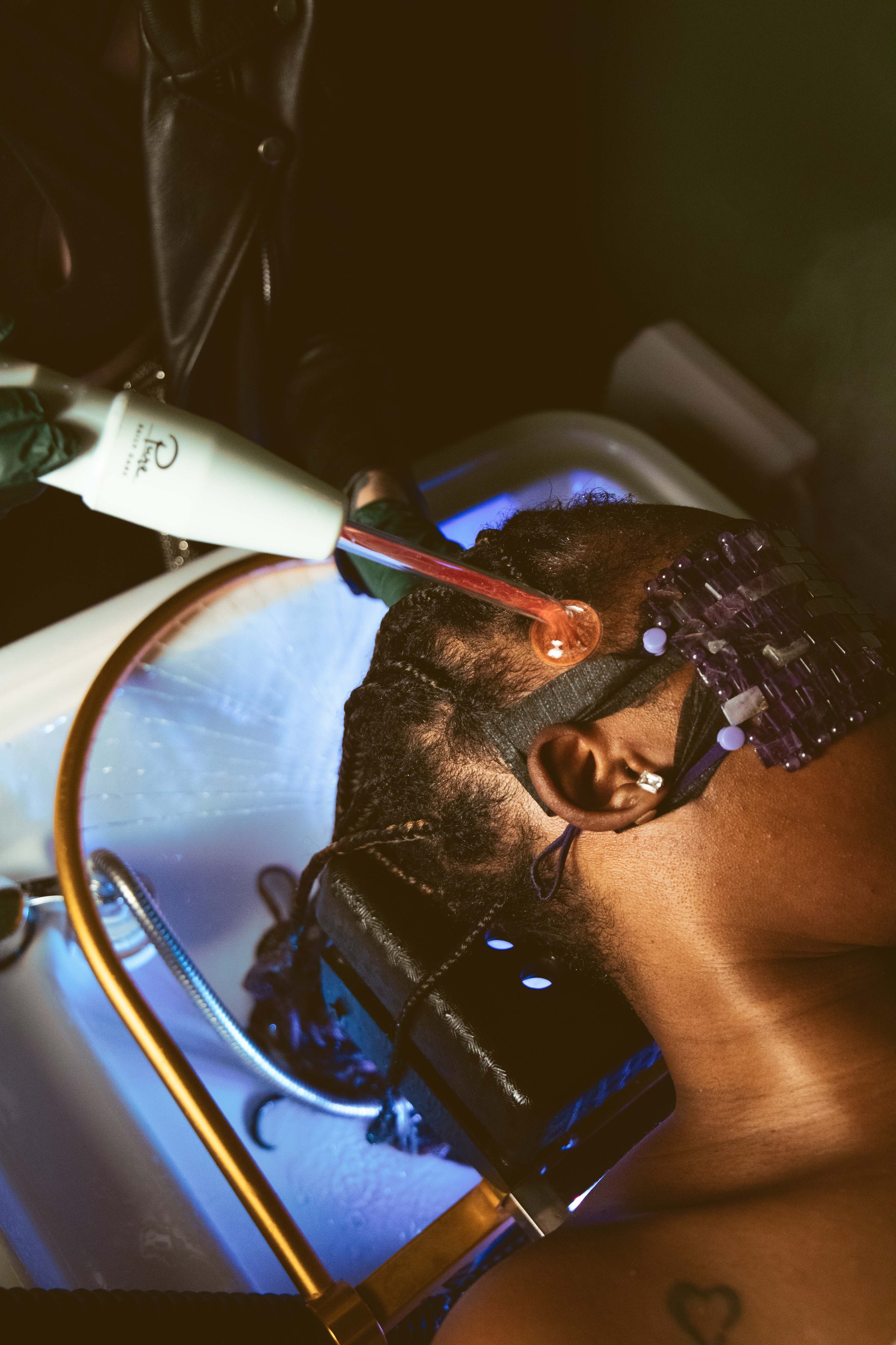 A person lying back in a dental chair getting a dental impression or mold taken of their upper teeth and gums with a purple tray in their mouth, while wearing a black protective apron and glasses.