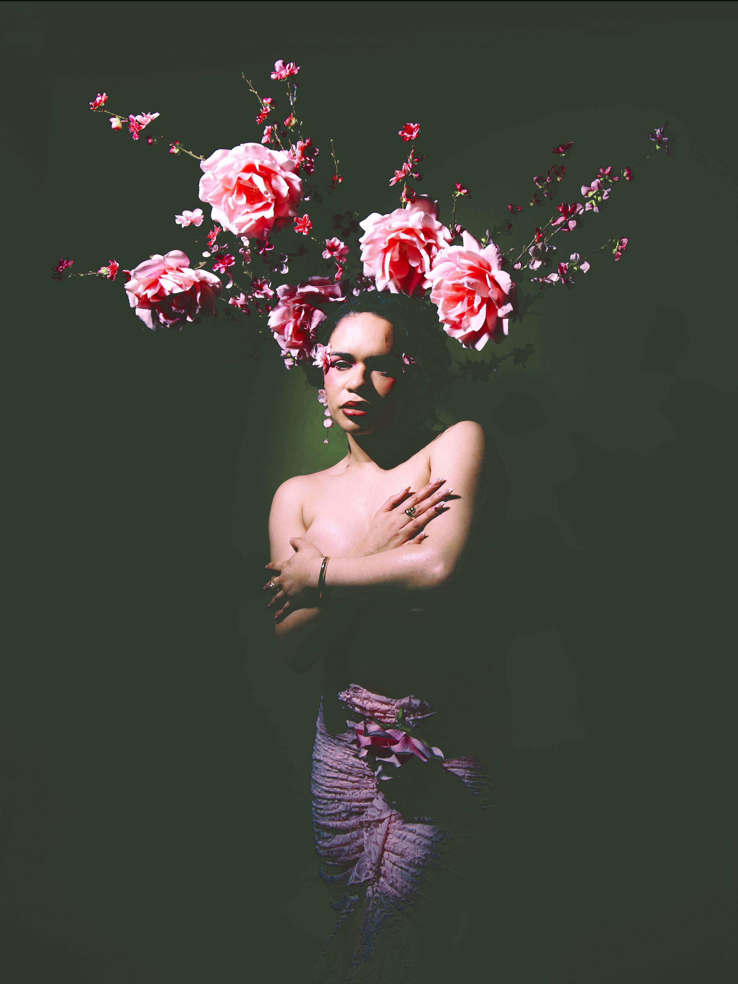 Local Dallas, Texas, DFW Non-traditional Fashion Editorial Creative Portraits Cover Art Photographer Photoshoot. Model Rosa Moran . A woman with a floral headdress and pink patterned shorts, standing against a dark green background.