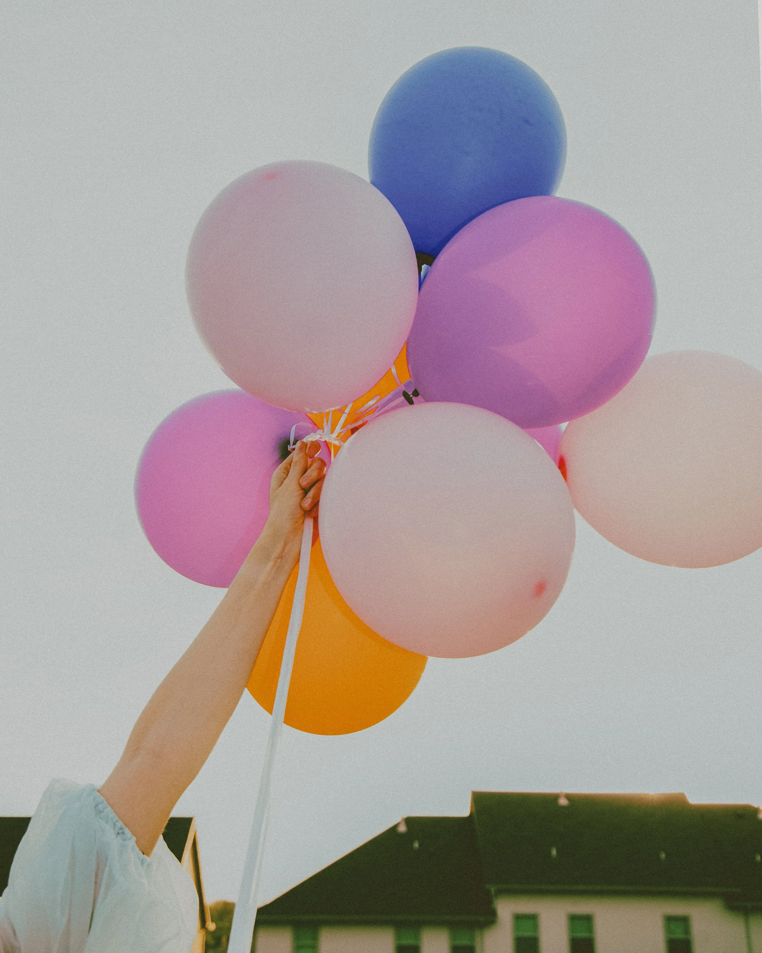 Local Dallas, Texas, DFW Non-traditional Fashion Editorial Creative Portraits Cover Art Photographer Photoshoot. A person holding a bunch of colorful balloons outdoors against a clear sky and a building with green windows.