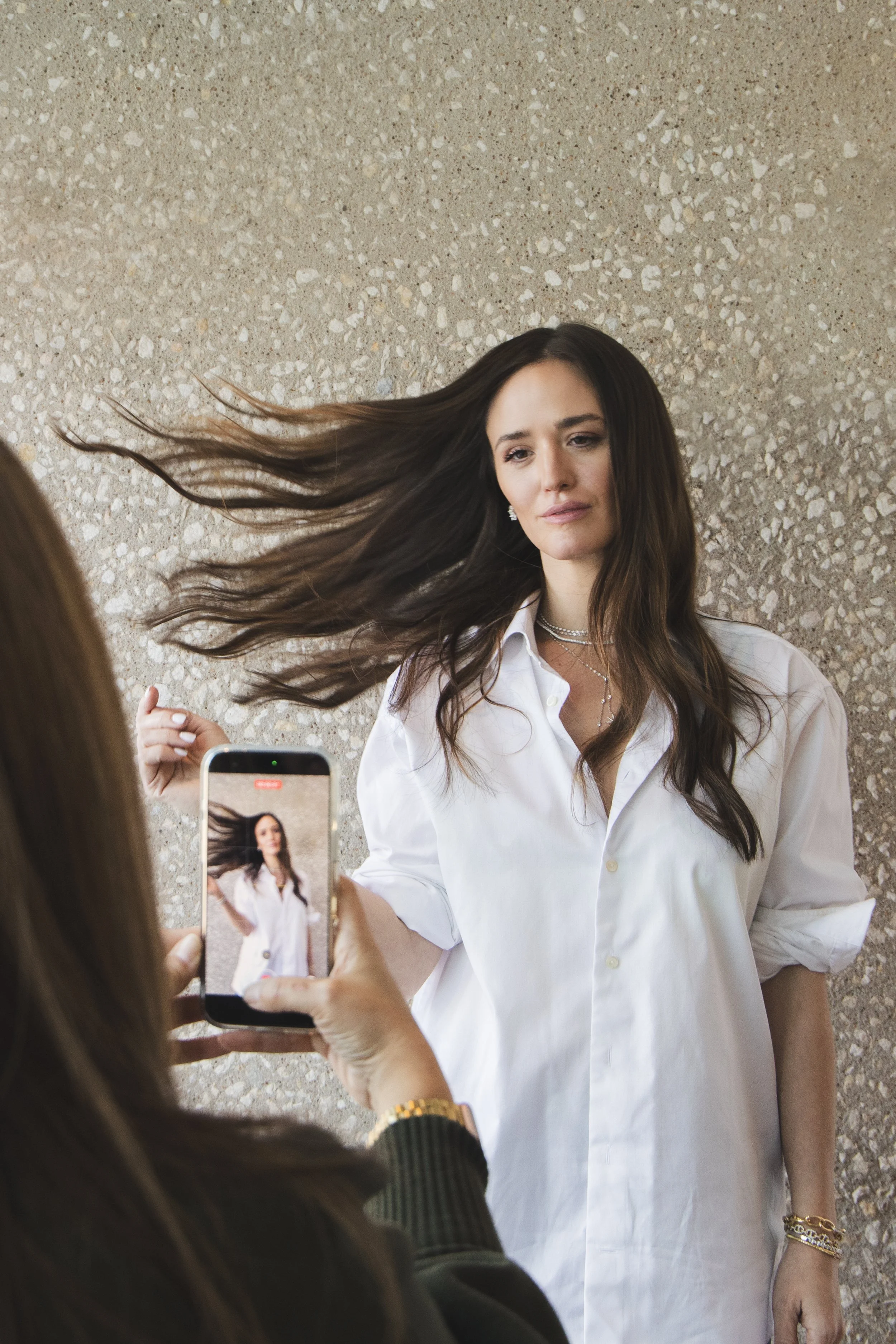 Woman with long dark hair lying on the ground, wearing a white shirt, posing for a photo taken by another person.