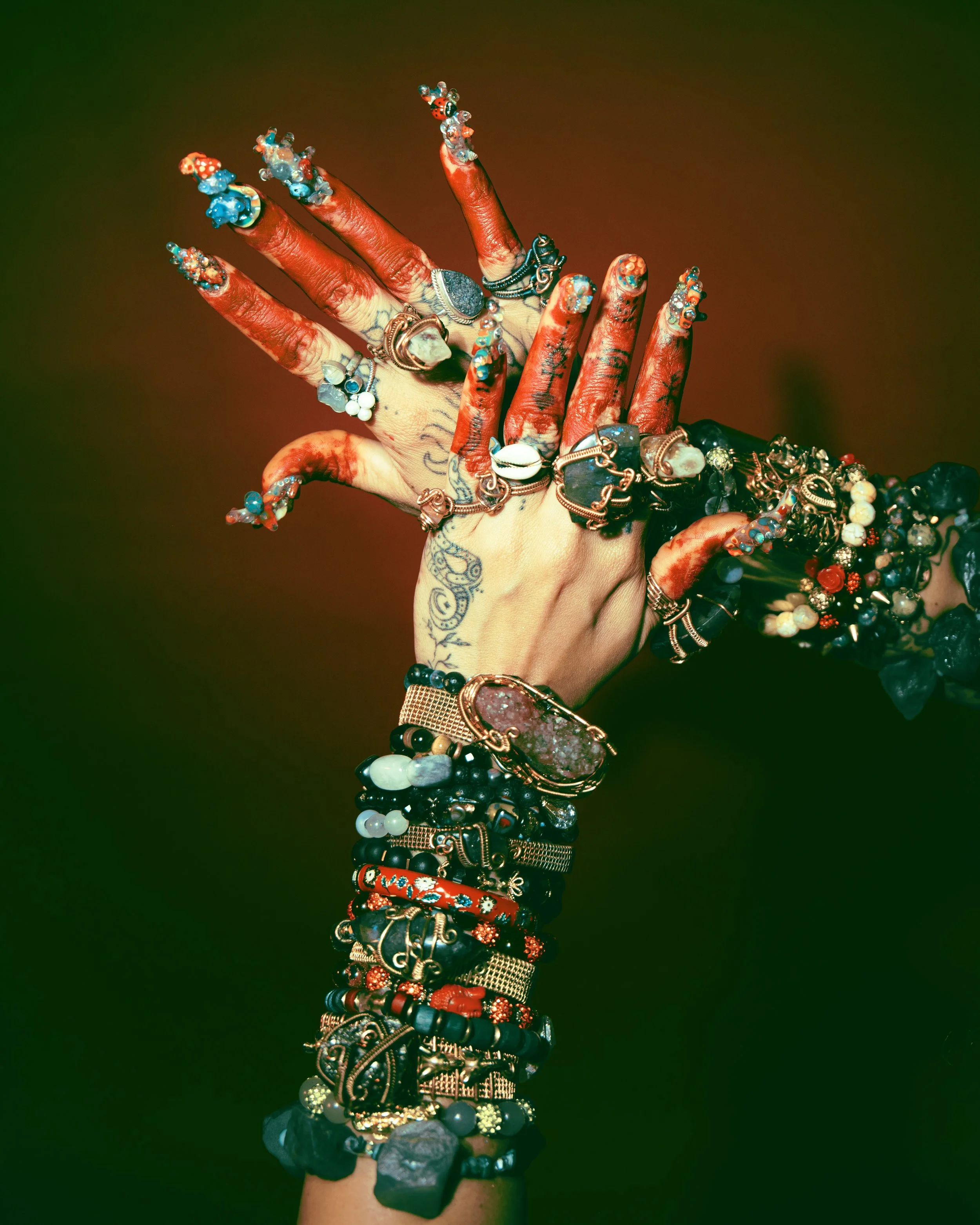 A hand adorned with numerous colorful rings, bracelets, and henna designs, with a dark background.