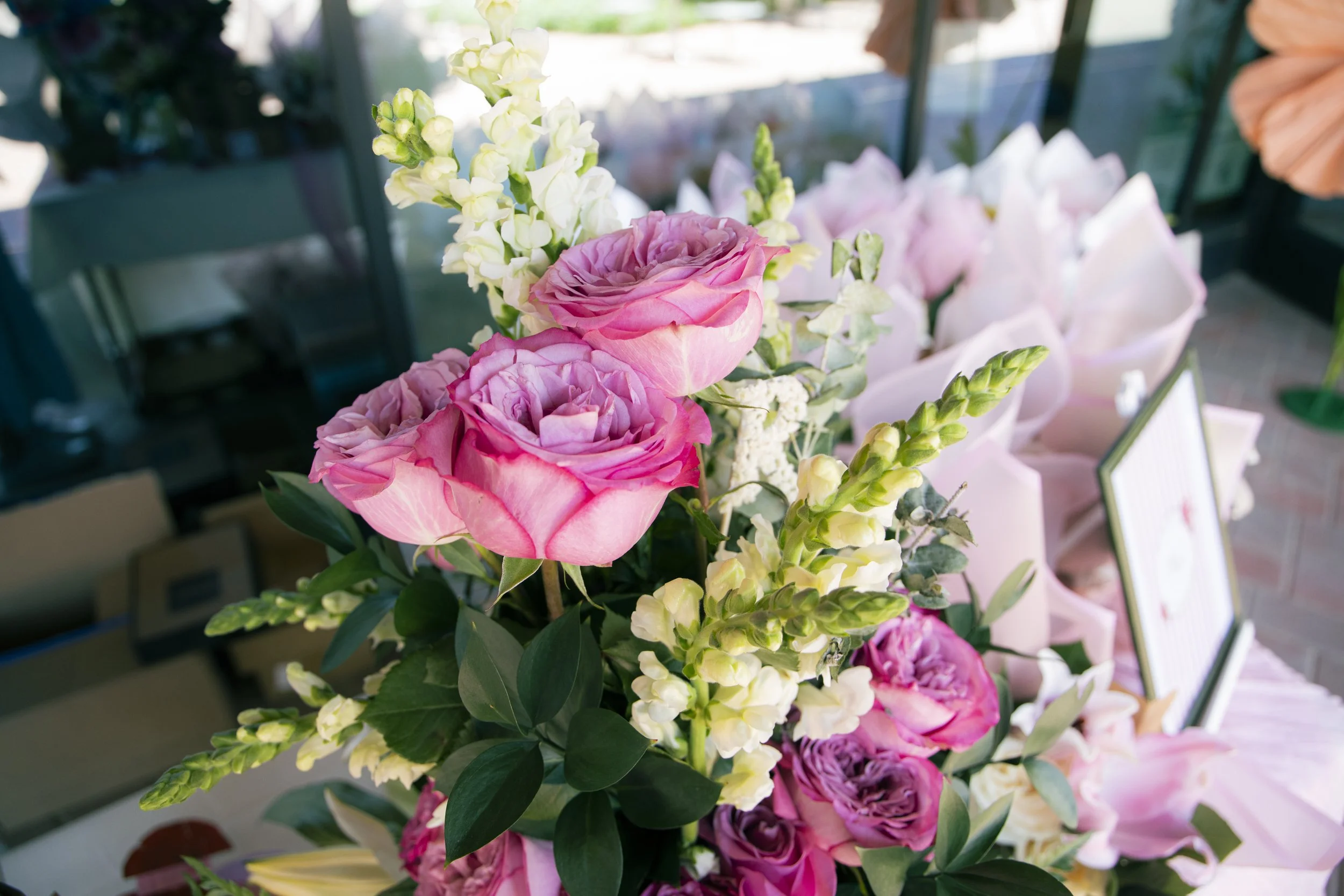 A bouquet of pink and white flowers, including roses and snapdragons, with green leaves in a floral arrangement.