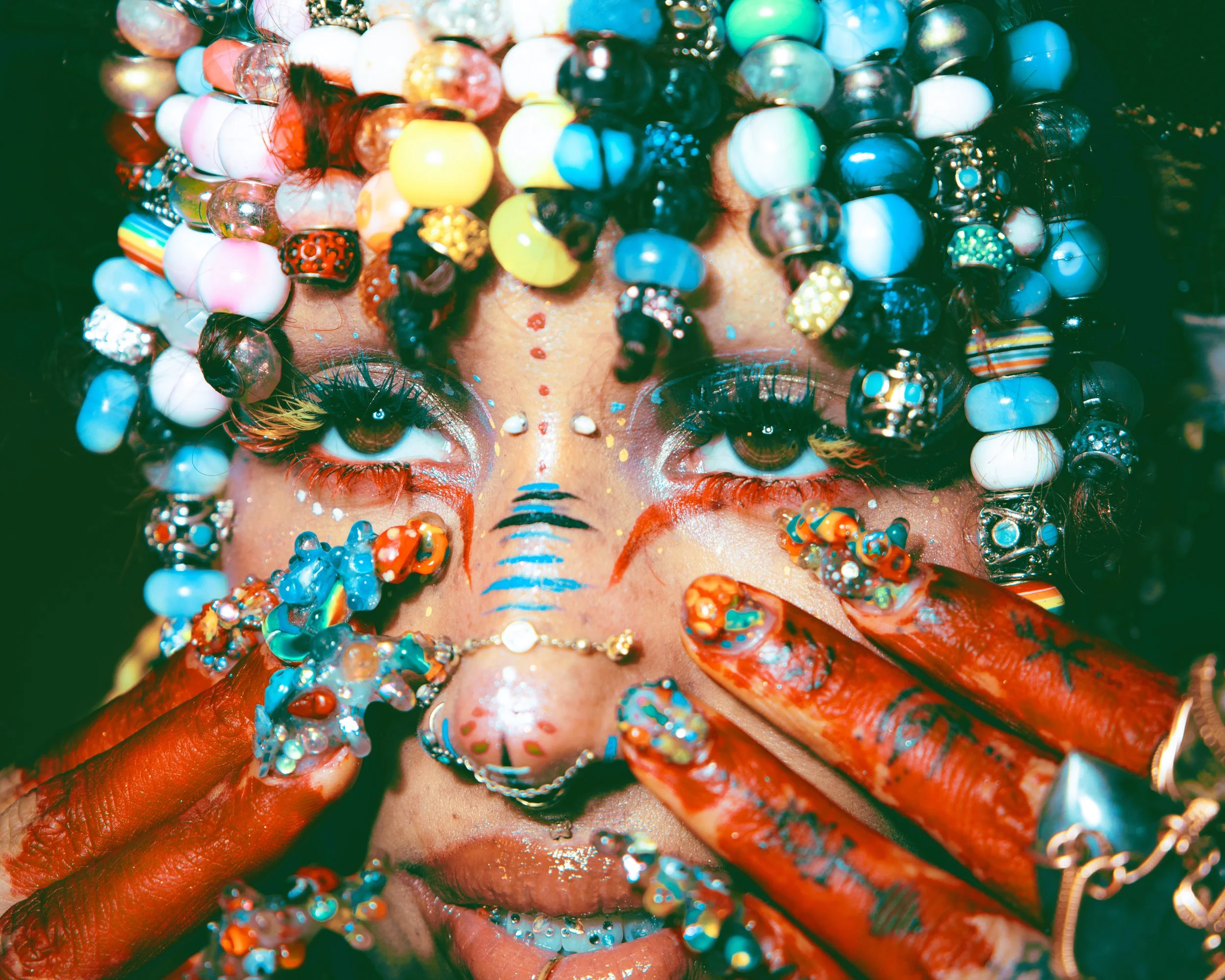Editorial creative portrait of Dallas, Texas local creative @marblle._ , wearing numerous colorful beads and jewelry, with their tongue sticking out at the camera, and an elaborate headpiece made of various beads, stones, and decorative elements. Non