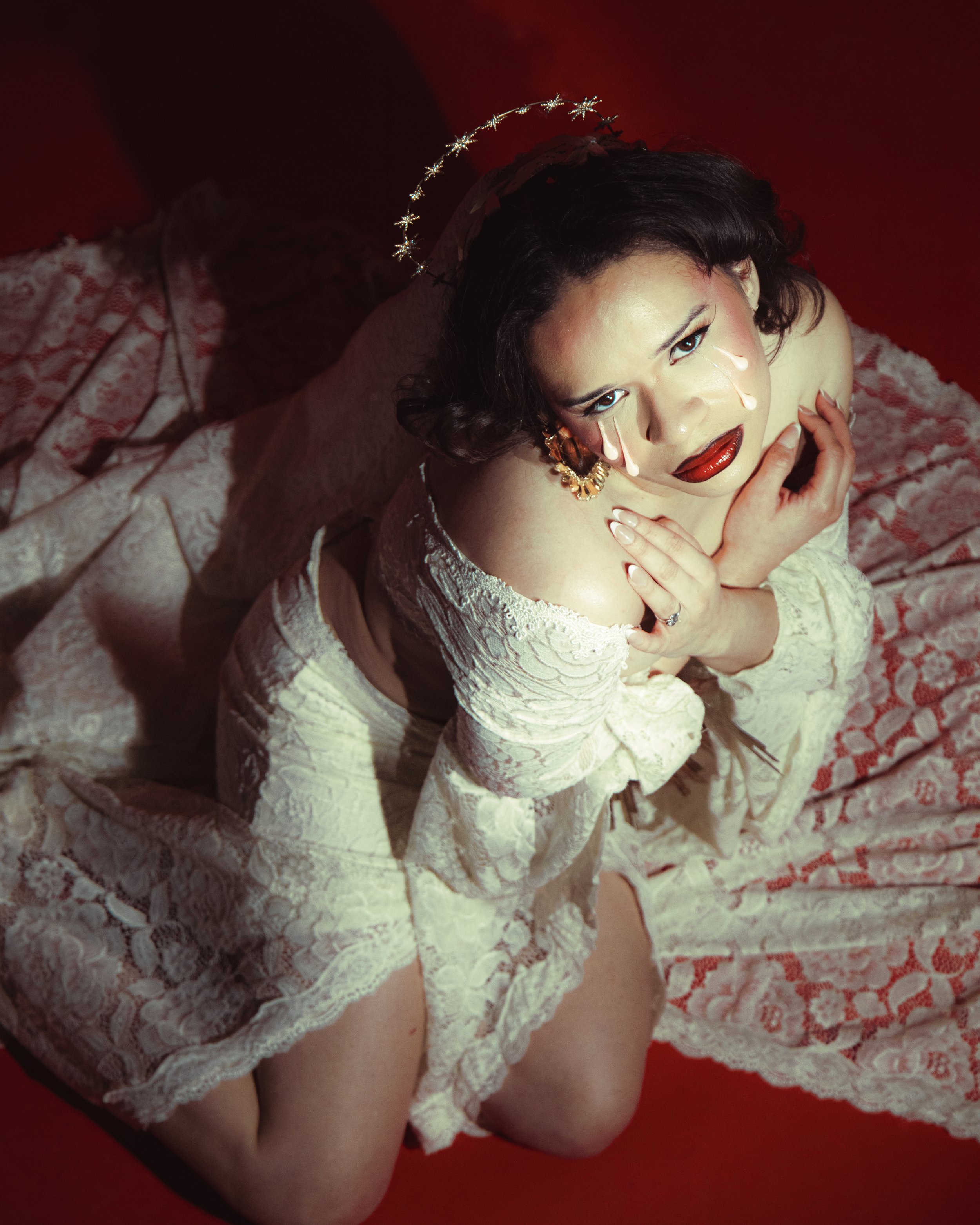 Local Dallas, Texas, DFW Non-traditional Fashion Editorial Creative Portraits Cover Art Photographer Photoshoot. A woman dressed in lace lingerie with bride accessories, including a veil and a floral headpiece, is posed on a red background. She is ga