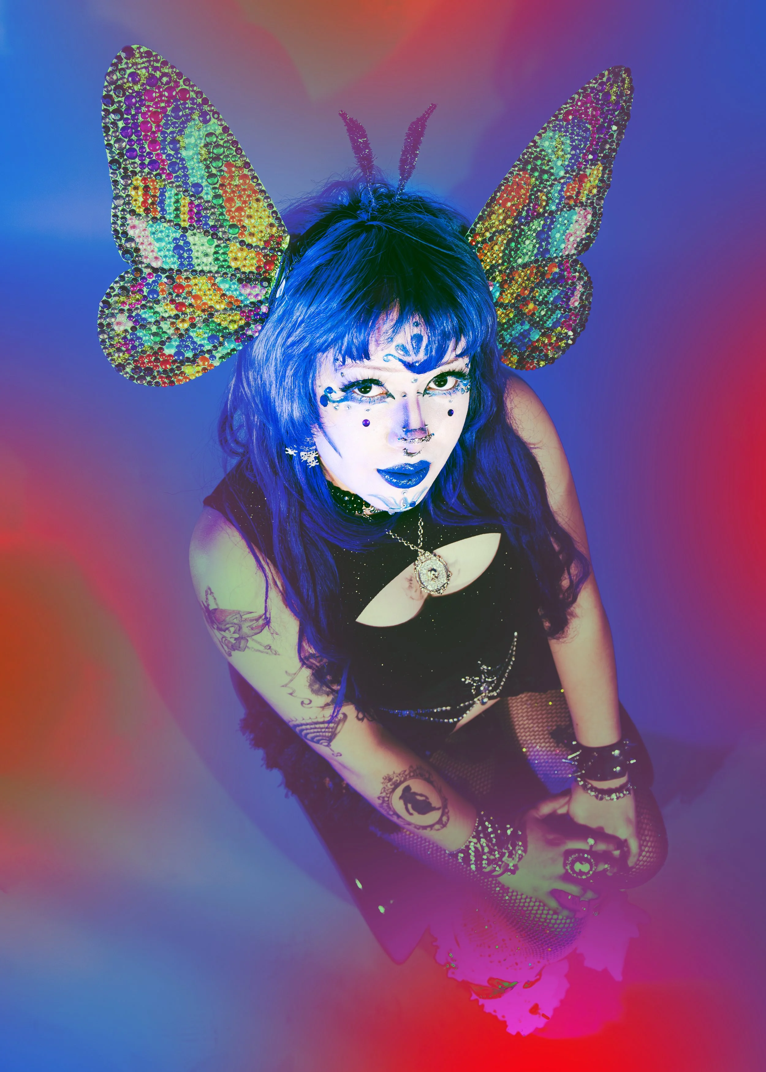 A woman in colorful makeup and accessories poses with large, glittery Local Dallas, Texas, DFW Non-traditional Editorial Creative Portraits Cover Art Photographer. Hair stylist, @seekingvivids . butterfly wings on her head, wearing fishnet stockings,