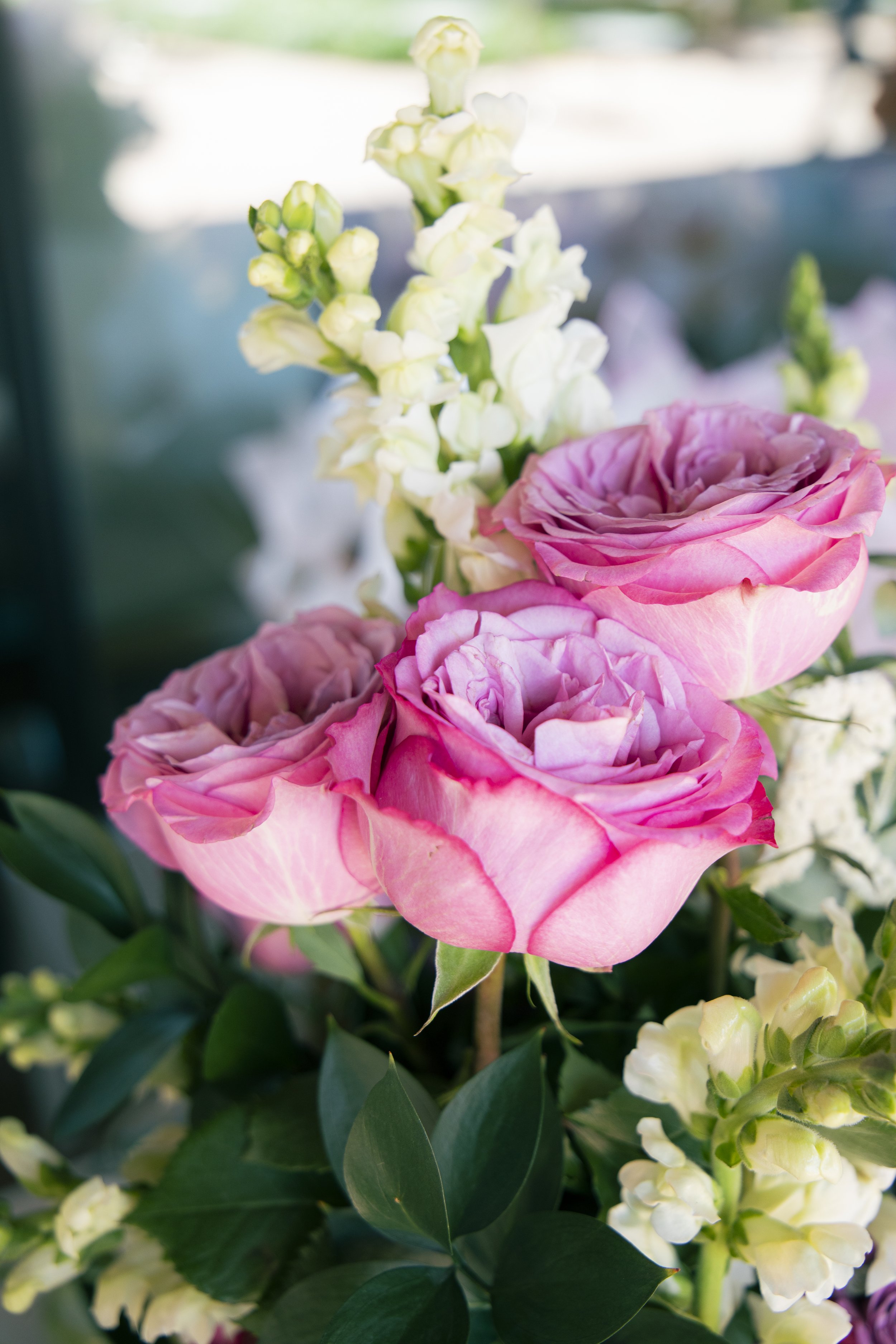 Close-up of pink roses and white lisianthus flowers with green leaves in a floral arrangement