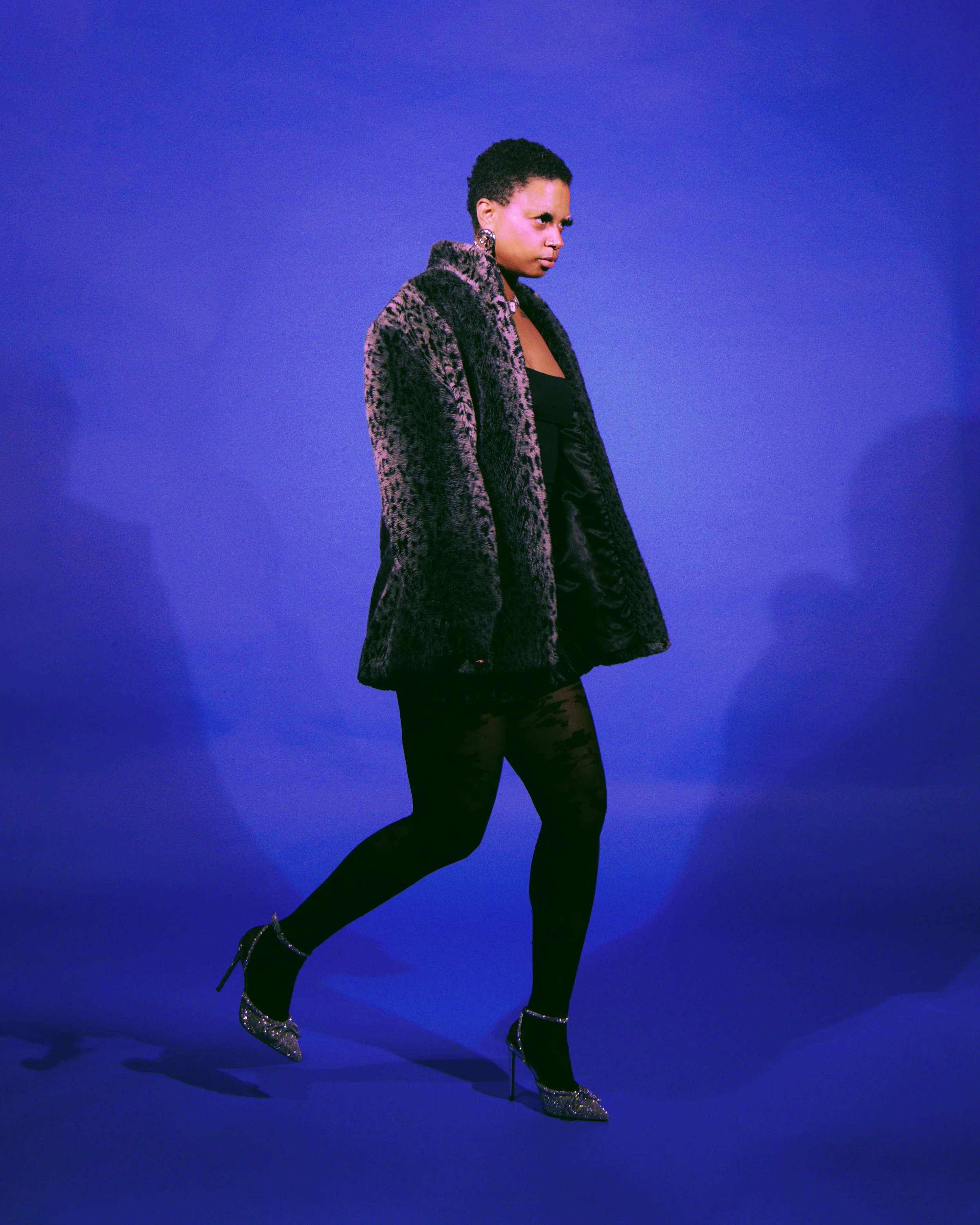 Local Dallas, Texas, DFW Non-traditional Fashion Editorial Creative Portraits Cover Art Photographer Photoshoot. A woman in a leopard print coat and high heels standing against a plain blue background.