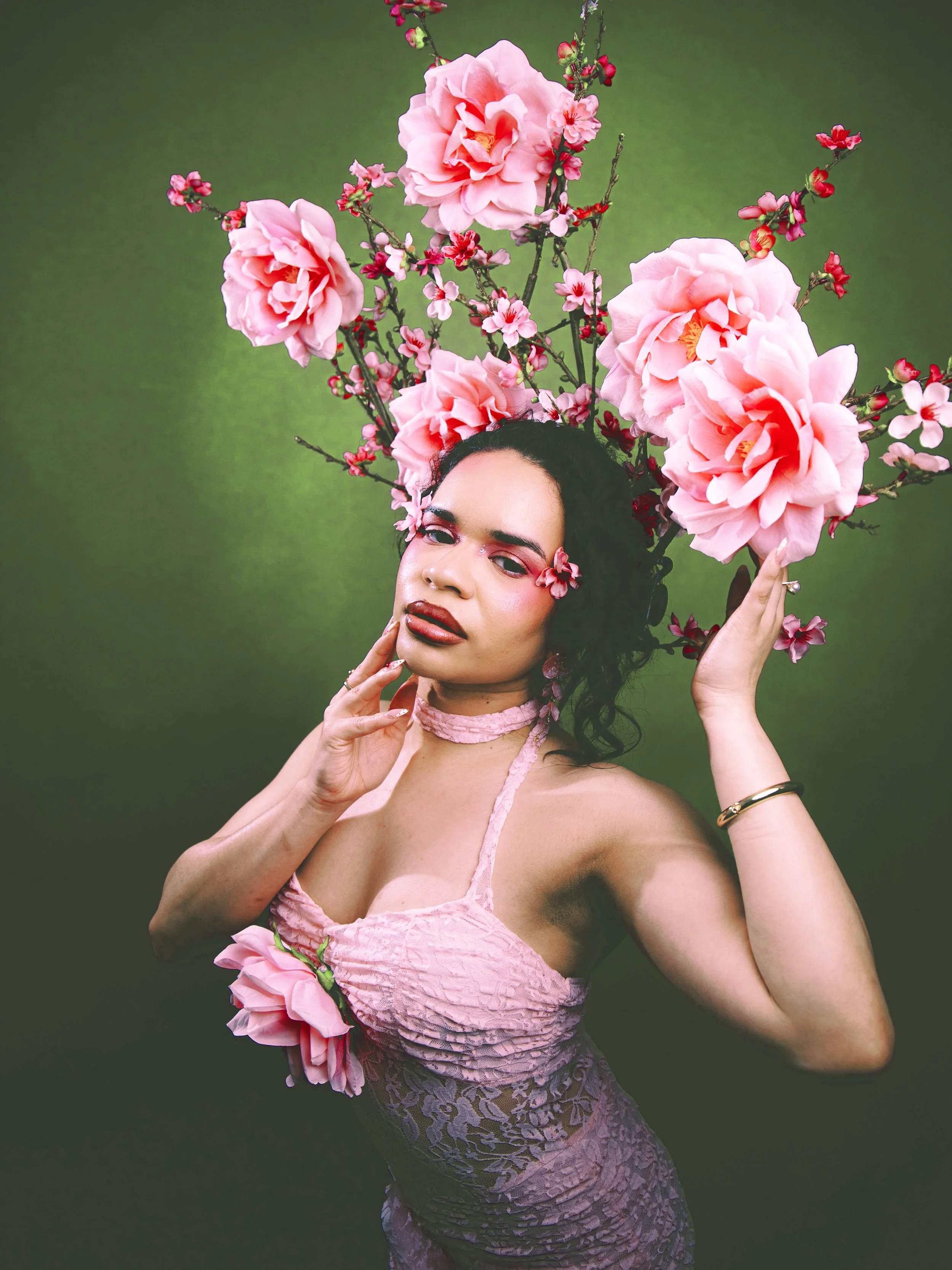 Local Dallas, Texas, DFW Non-traditional Fashion Editorial Creative Portraits Cover Art Photographer Photoshoot. @roseypears . A woman with curly dark hair and makeup is posing with large pink flowers arranged as a headdress and on her clothing again