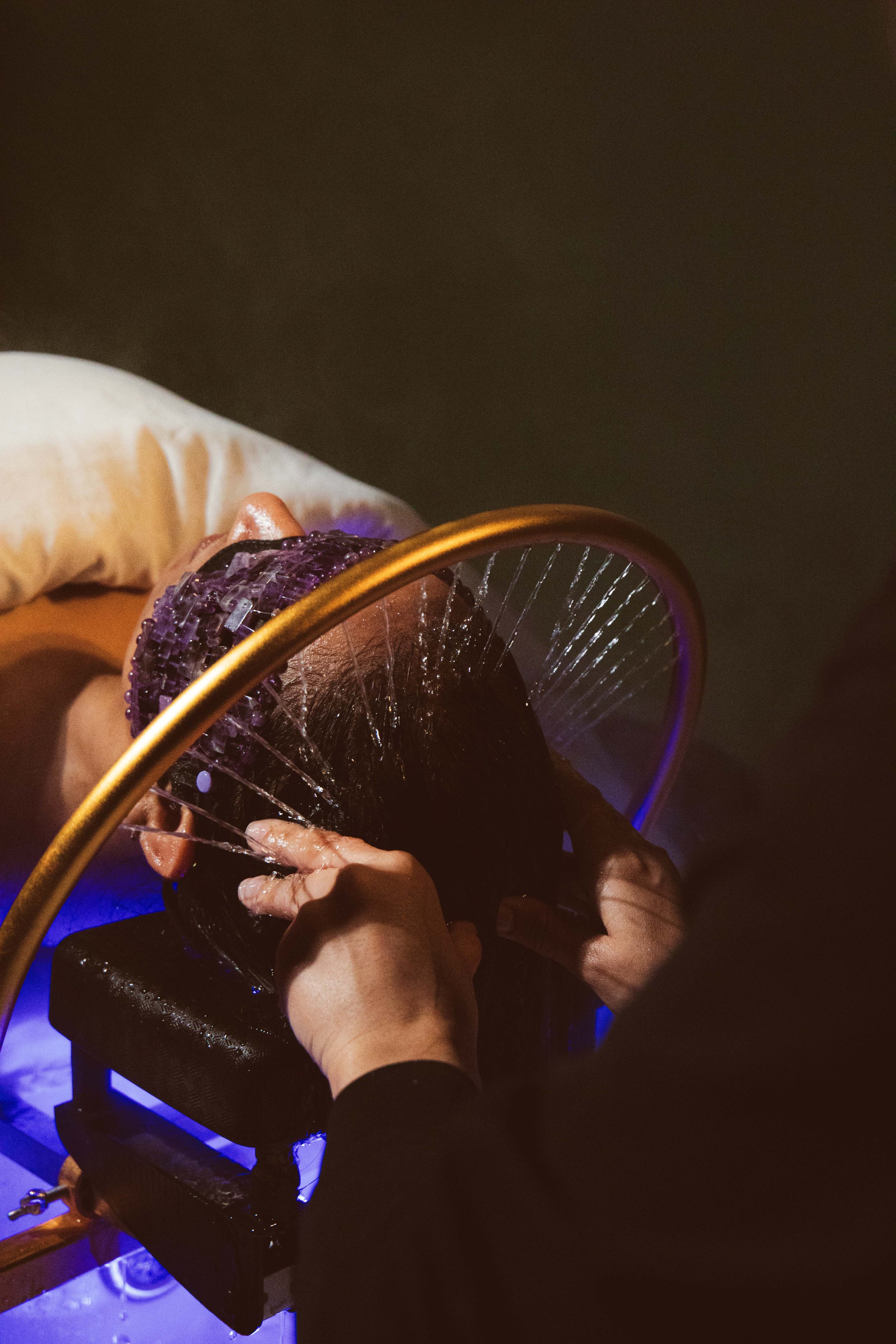 Person receiving a manicure, with hands resting on a black cushioned surface, a purple LED light, and a glow from a nearby device.