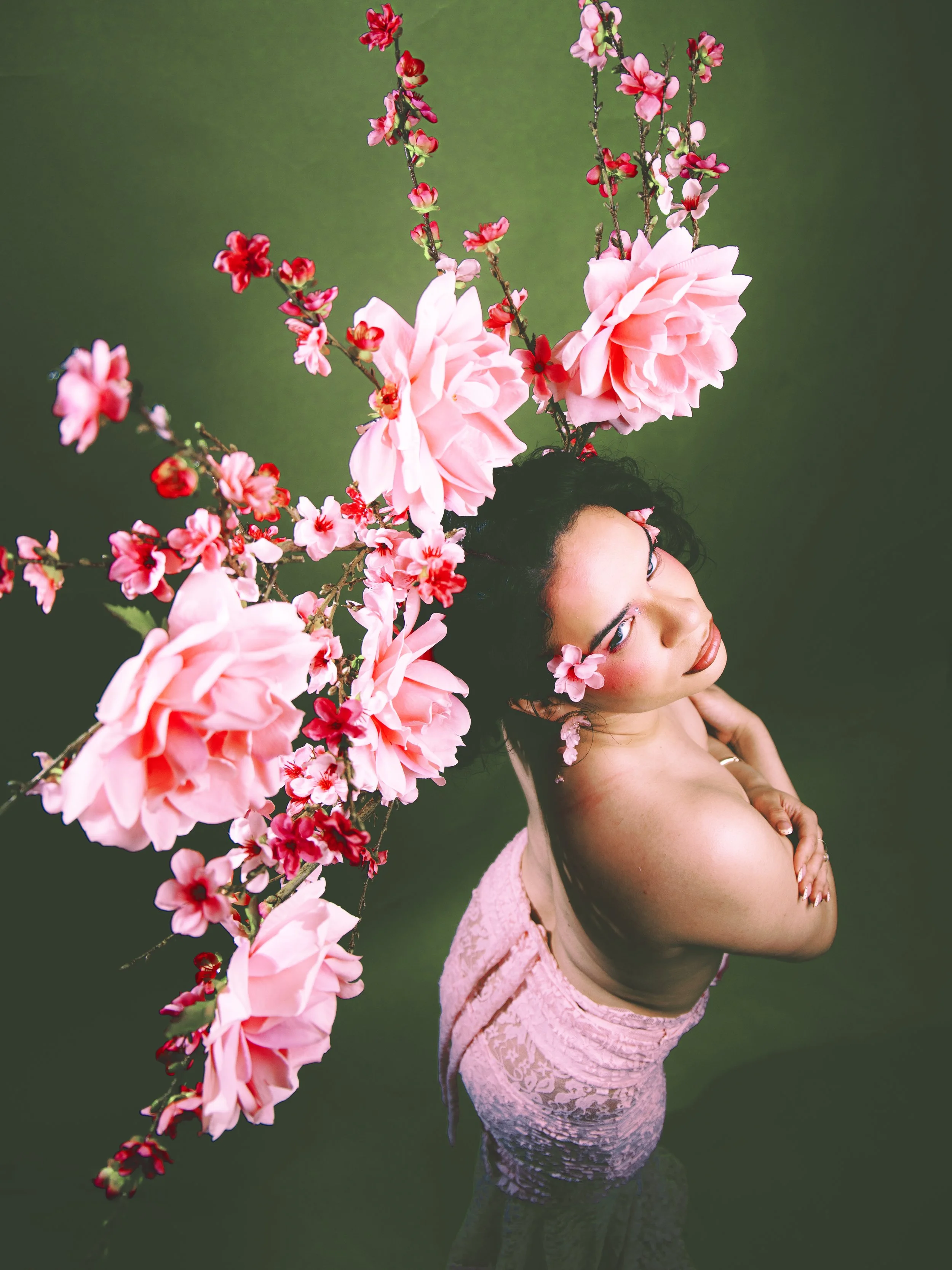 Local Dallas, Texas, DFW Non-traditional Editorial Creative Portraits Cover Art Photographer. Creative portrait of local Dallas, Texas model, @roseypears . A woman in a pink lace dress poses with pink and red flowers, with a green background.