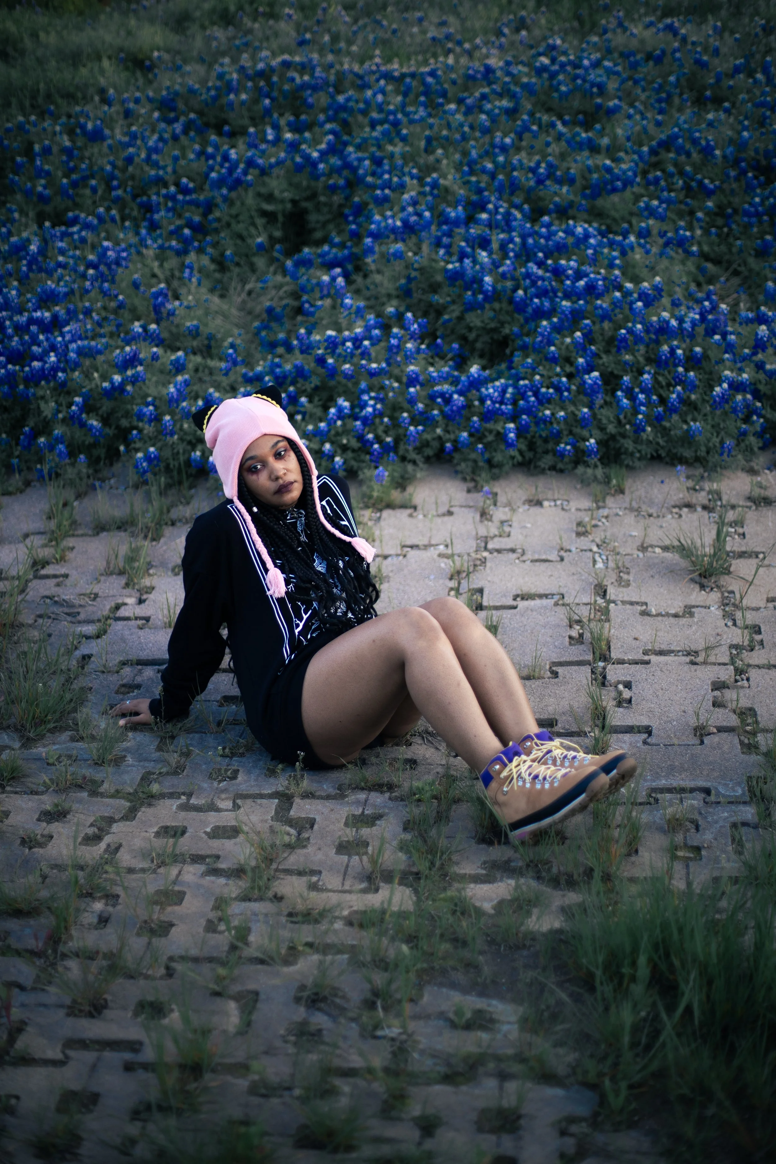 Local Dallas, Texas, DFW Non-traditional Fashion Editorial Creative Portraits Cover Art Photographer Photoshoot. Musician Igimeji . A young woman with dark braided hair, wearing a pink hat with animal ears, a black jacket with white stripes, and tan 