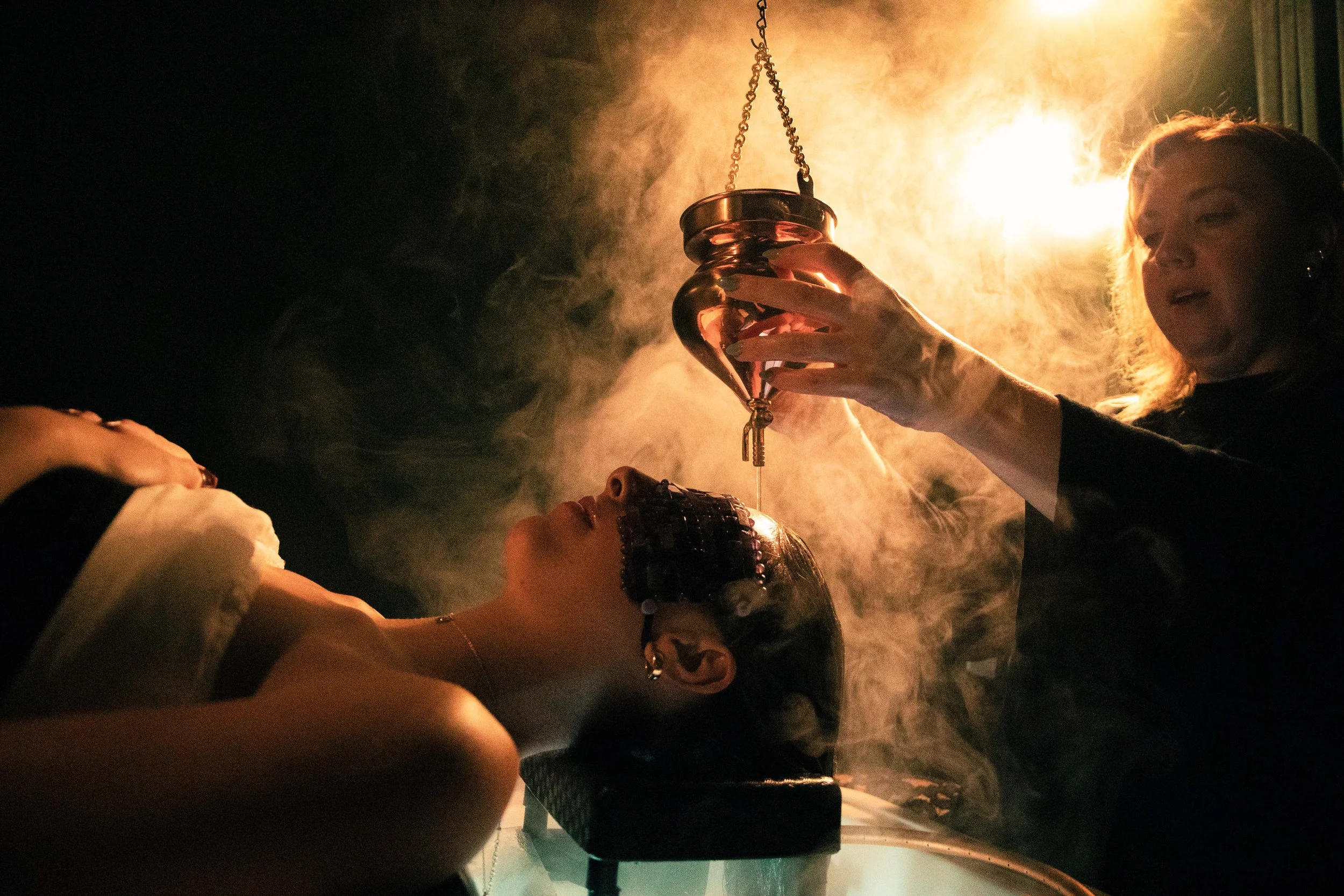 A person holding a lantern with a fire inside, surrounded by fog and warm lighting, with only part of their face visible.