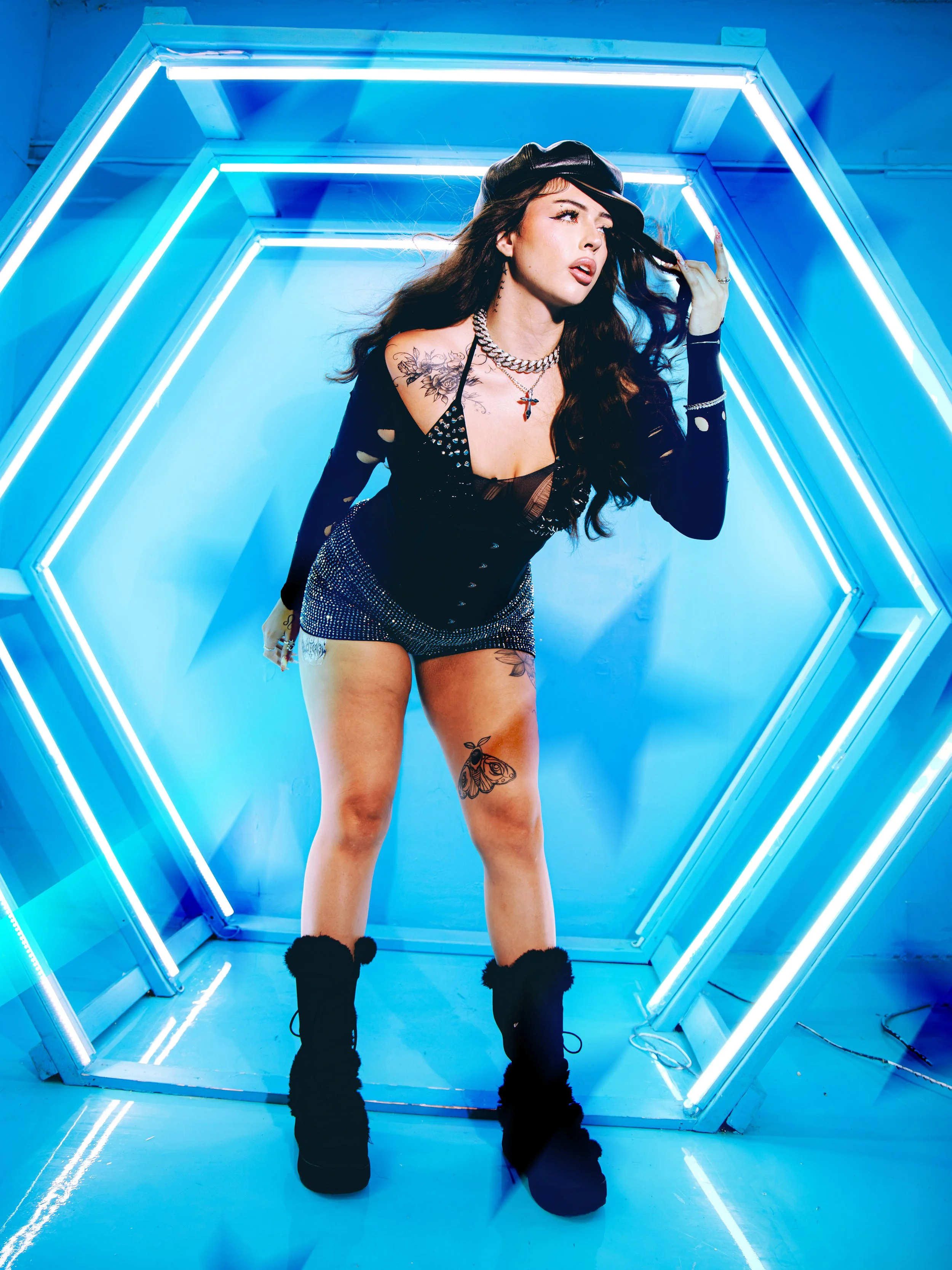 Local Dallas, Texas, DFW Non-traditional Fashion Editorial Creative Portraits Cover Art Photographer Photoshoot. A woman with long dark hair, tattoos, and gold jewelry stands inside a hexagon-shaped neon-lit tunnel in a pose with one hand touching he