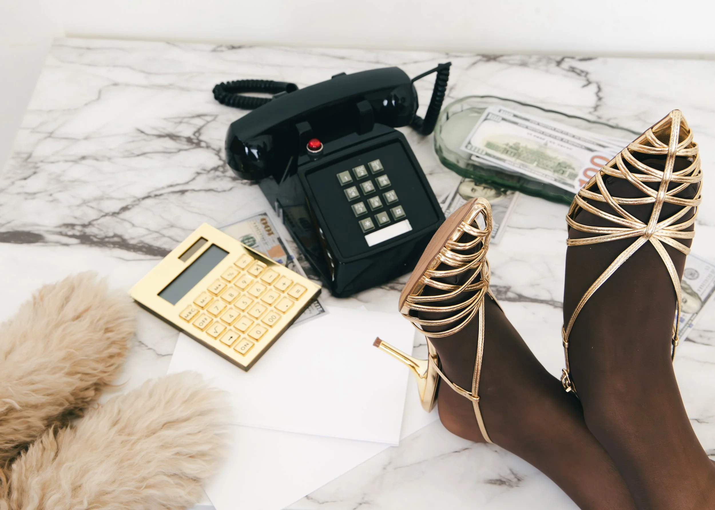 Local Dallas, Texas, DFW Non-traditional Fashion Editorial Creative Portraits Cover Art Photographer Photoshoot. Flat lay of a black landline telephone, a yellow calculator, a stack of hundred-dollar bills, a glass bottle with papers, a pair of gold 