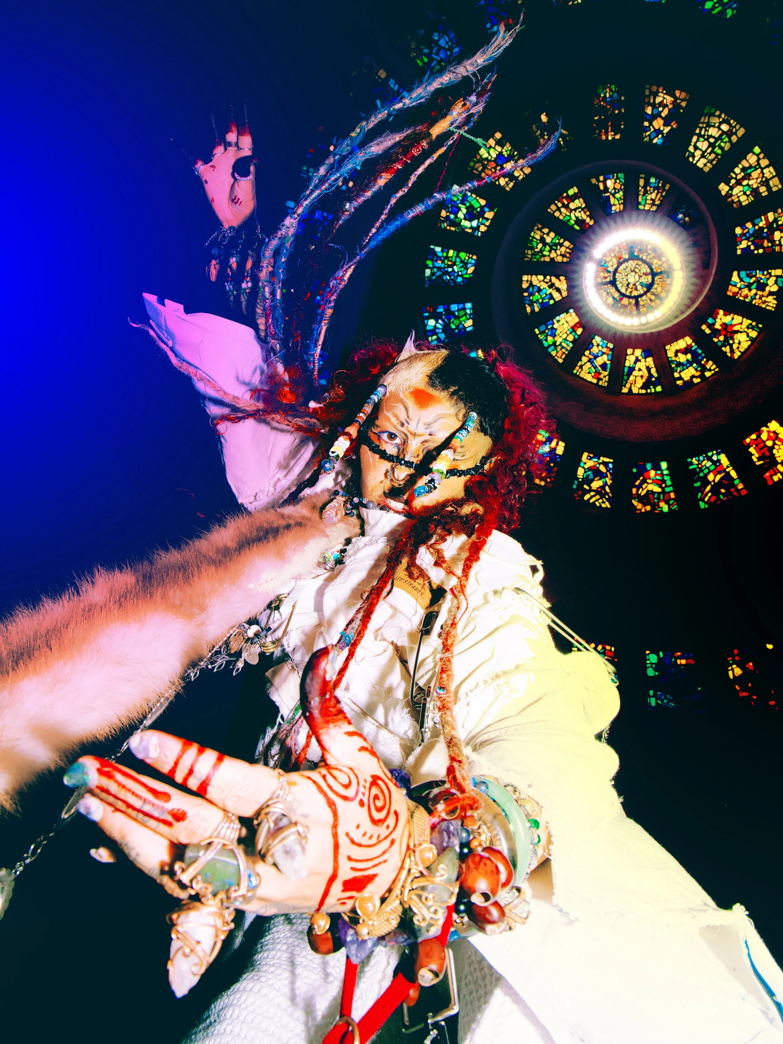 Local Dallas, Texas, DFW Non-traditional Editorial Creative Portraits Cover Art Photographer. @marblle._ This image features a person with vibrant, colorful accessories in front of a large, circular stained glass window. The individual has elaborate 