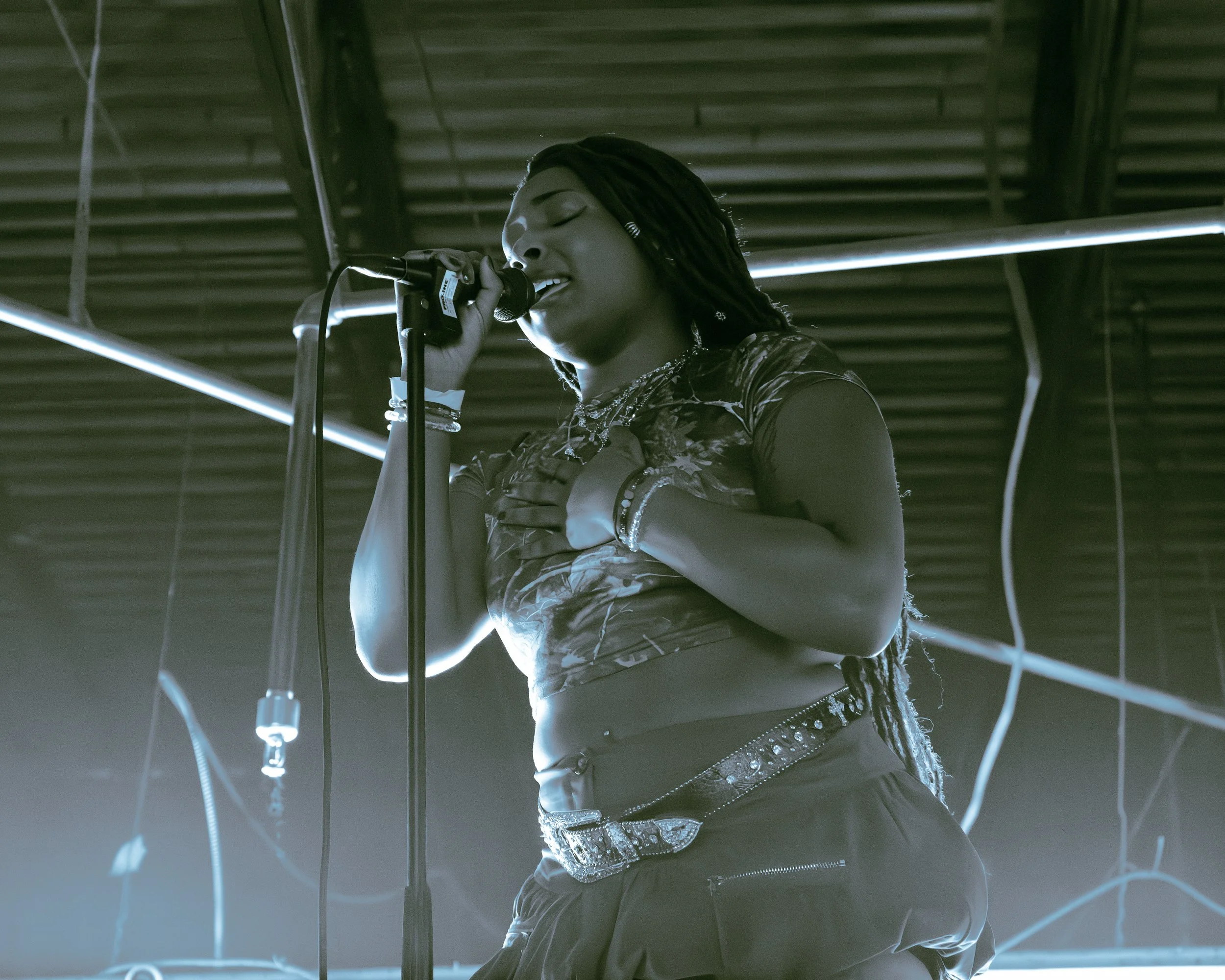 Local Dallas, Texas, DFW Non-traditional Fashion Editorial Creative Portraits Cover Art Photographer Photoshoot. Musician @ Seihara . A woman with dreadlocks singing into a microphone on stage, dressed in a shiny, patterned outfit with jewelry, under