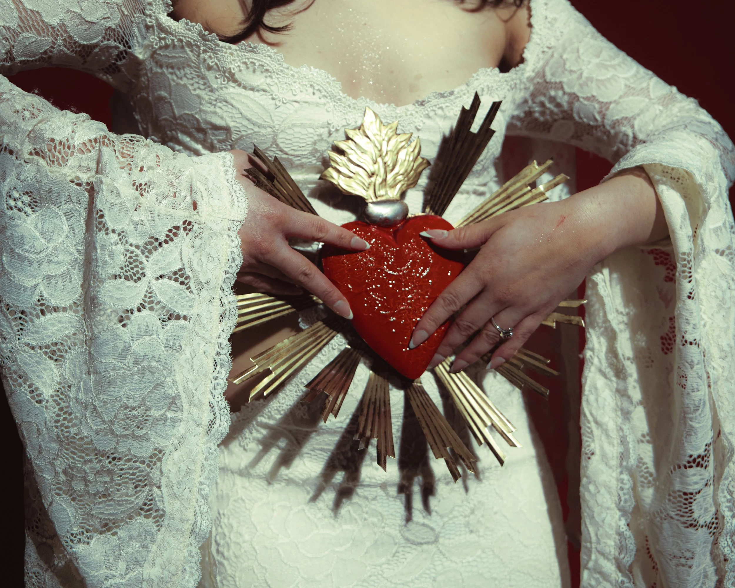 Local Dallas, Texas, DFW Non-traditional Fashion Editorial Creative Portraits Cover Art Photographer Photoshoot. A person wearing a white lace dress holding a decorative heart-shaped object with a gold leaf ornament on top, gold rays fanning outward 
