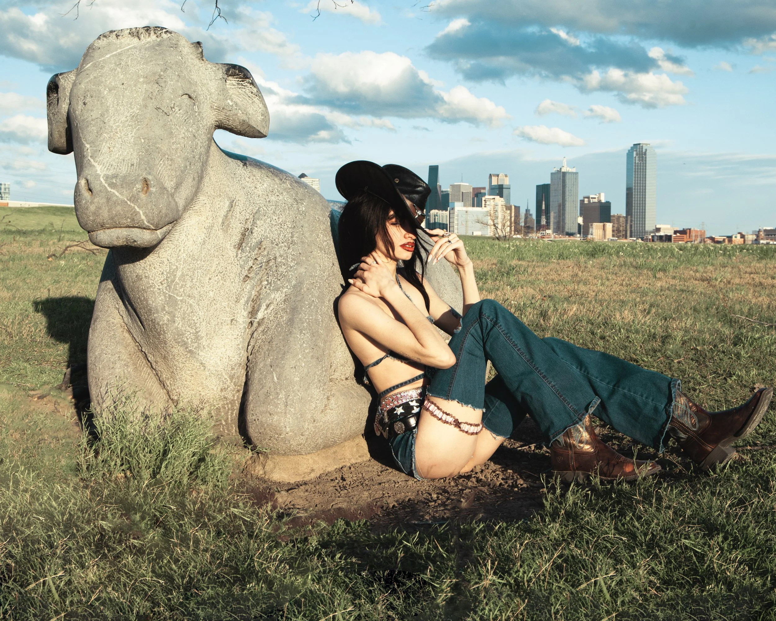 Local Dallas, Texas, DFW Non-traditional Fashion Editorial Creative Portraits Cover Art Photographer Photoshoot. Trammell Crow Park . A woman with dark hair, red lipstick, and tattooed arms sits on the grass leaning against a large stone sculpture of
