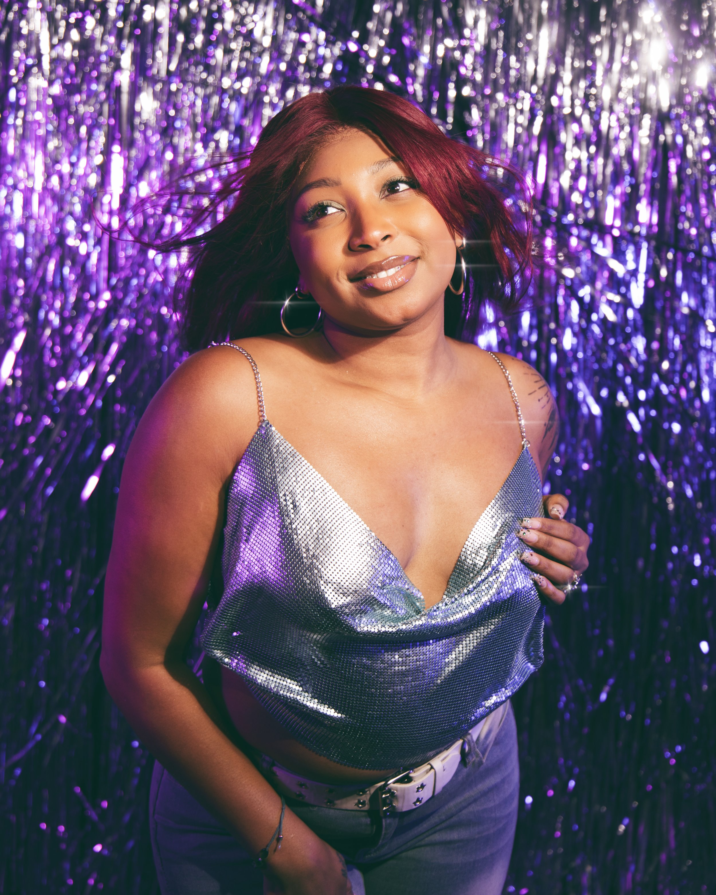 Local Dallas, Texas, DFW Non-traditional Fashion Editorial Creative Portraits Cover Art Photographer Photoshoot. Musician Seihara . A woman with medium skin tone and wavy dark red hair smiling at camera, wearing a silver sequin top and hoop earrings,