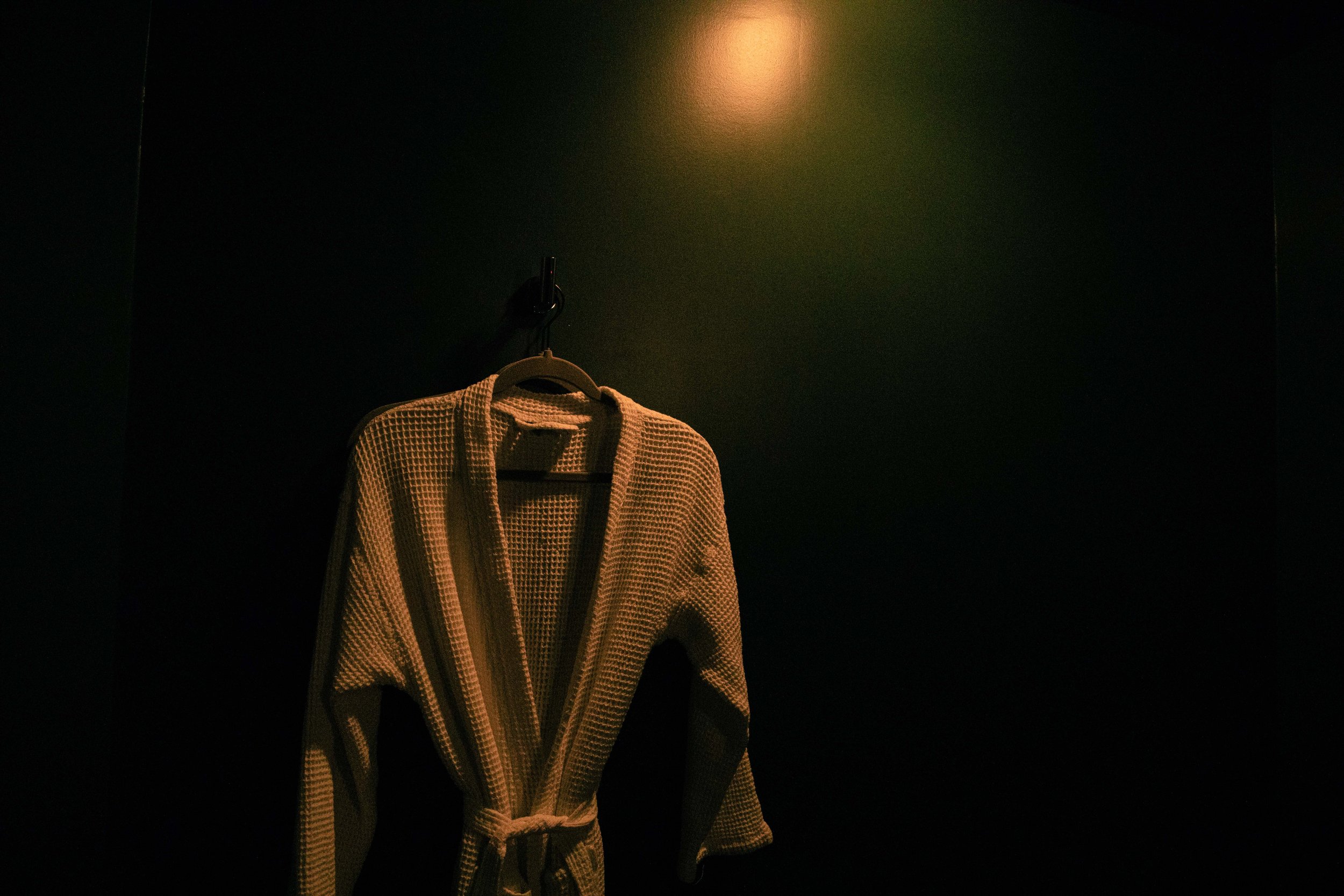 A tan checkered bathrobe hanging on a hook on a dark green wall, illuminated by a warm light overhead.