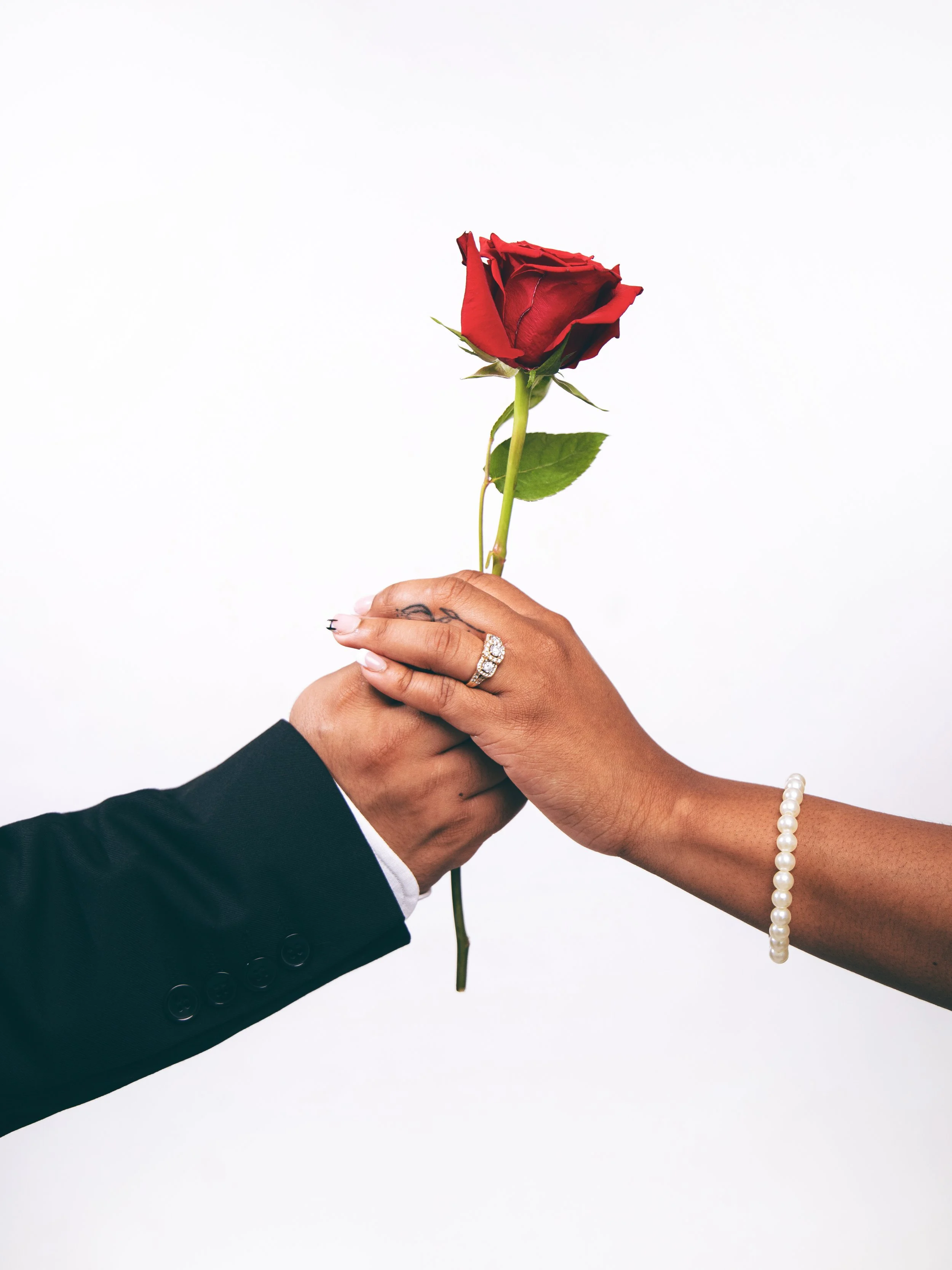 Local Dallas, Texas, DFW Non-traditional Fashion Editorial Creative Portraits Cover Art Photographer Photoshoot. Wedding Details. A person in a suit hands a woman a red rose against a plain white background.