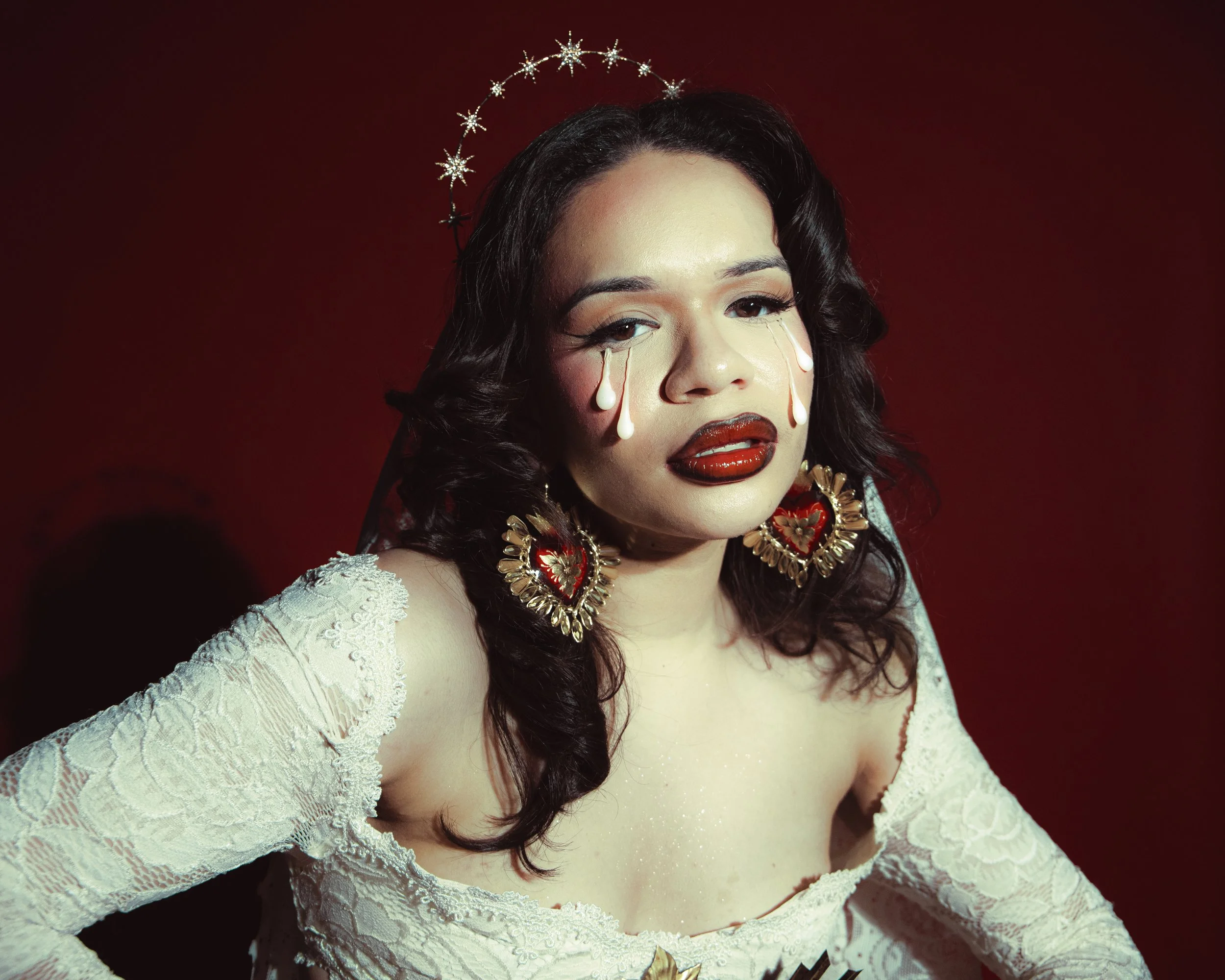 Local Dallas, Texas, DFW Non-traditional Fashion Editorial Creative Portraits Cover Art Photographer Photoshoot. A woman with dark, curly hair wearing a white lace dress and jewelry, including large gold earrings and a large gold necklace, against a 