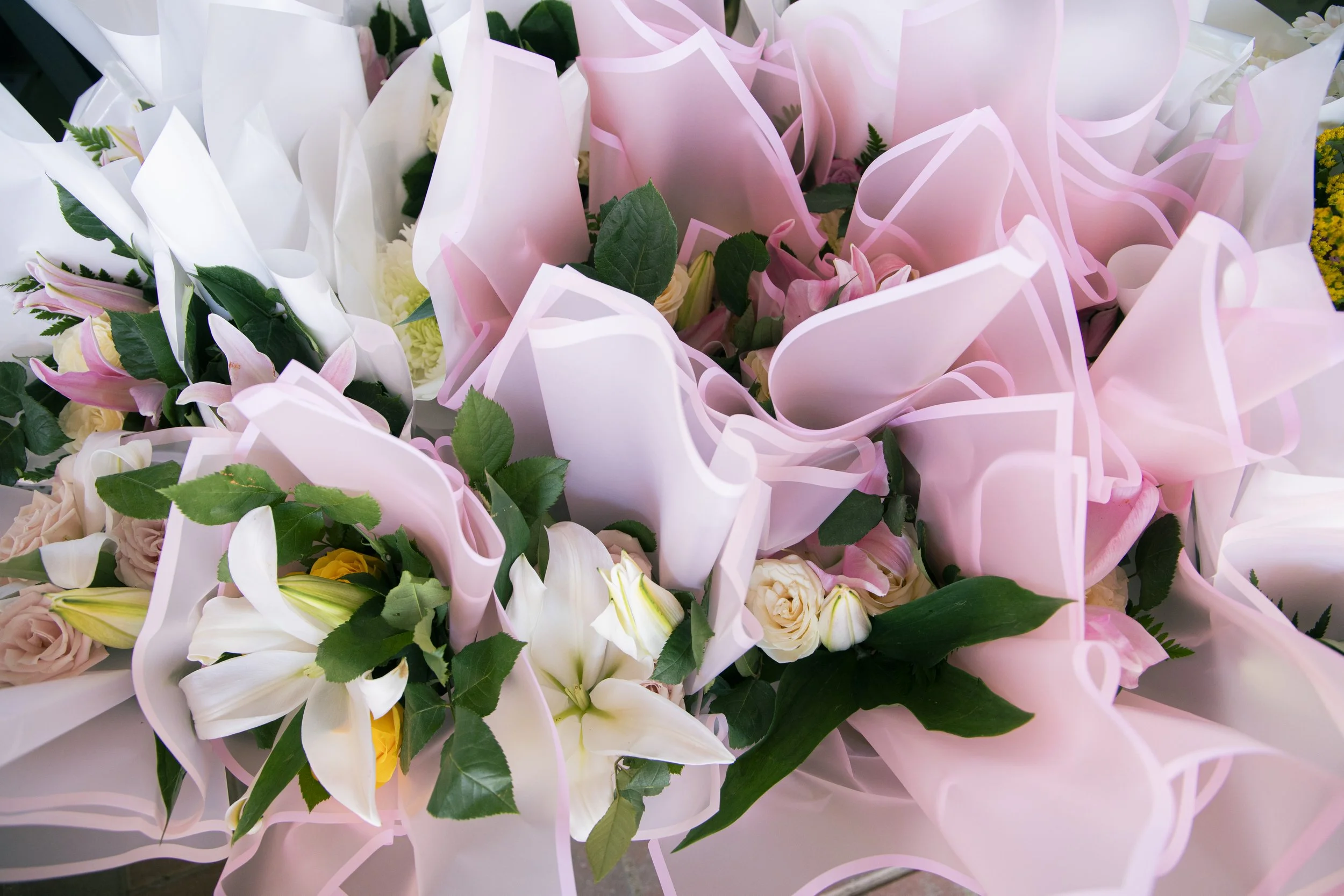 Close-up of a bouquet of pink, white, and yellow flowers wrapped in pink and white paper.