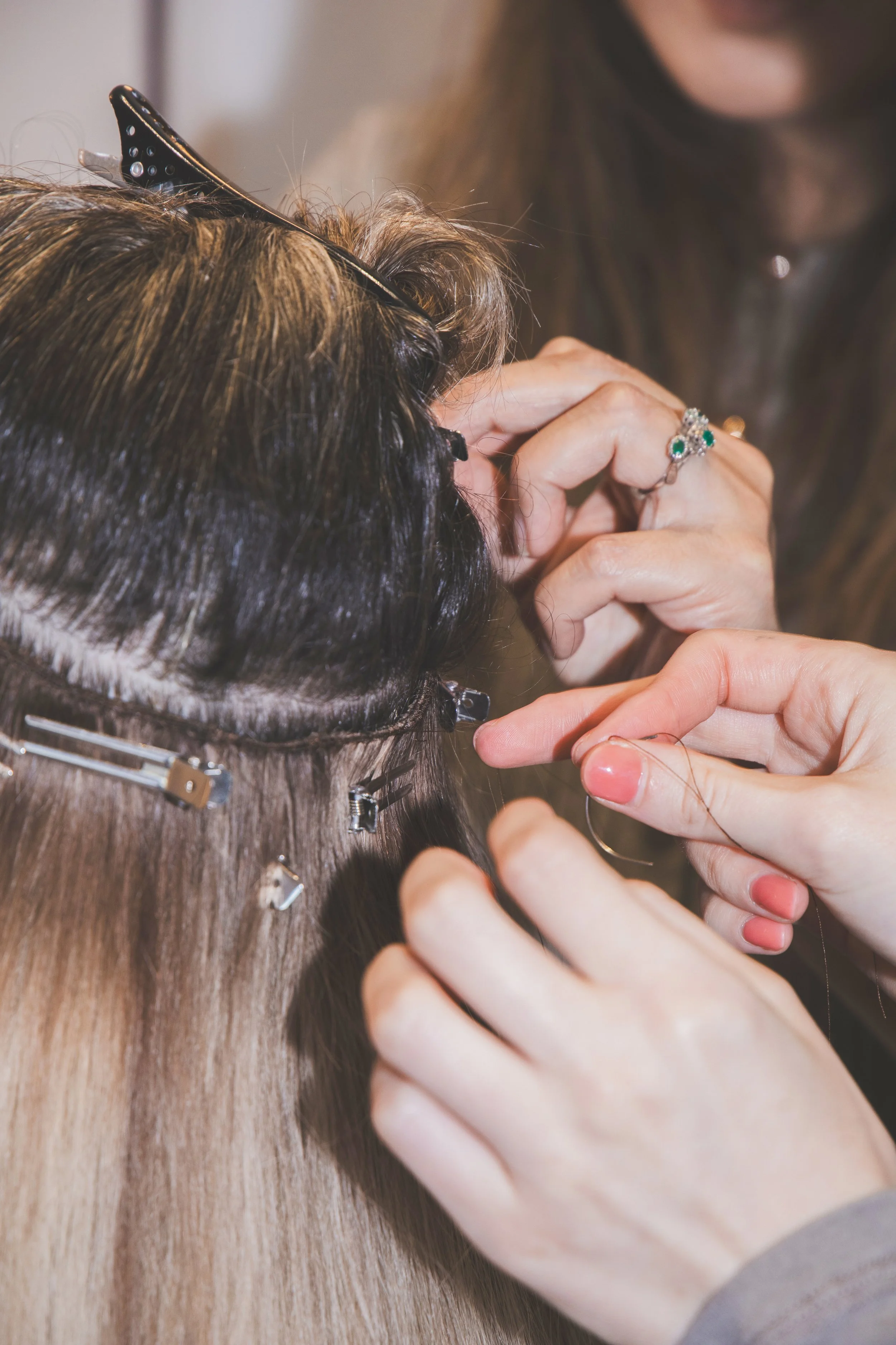 Person styling a person's hair with clips and jewelry in a salon or styling setting.