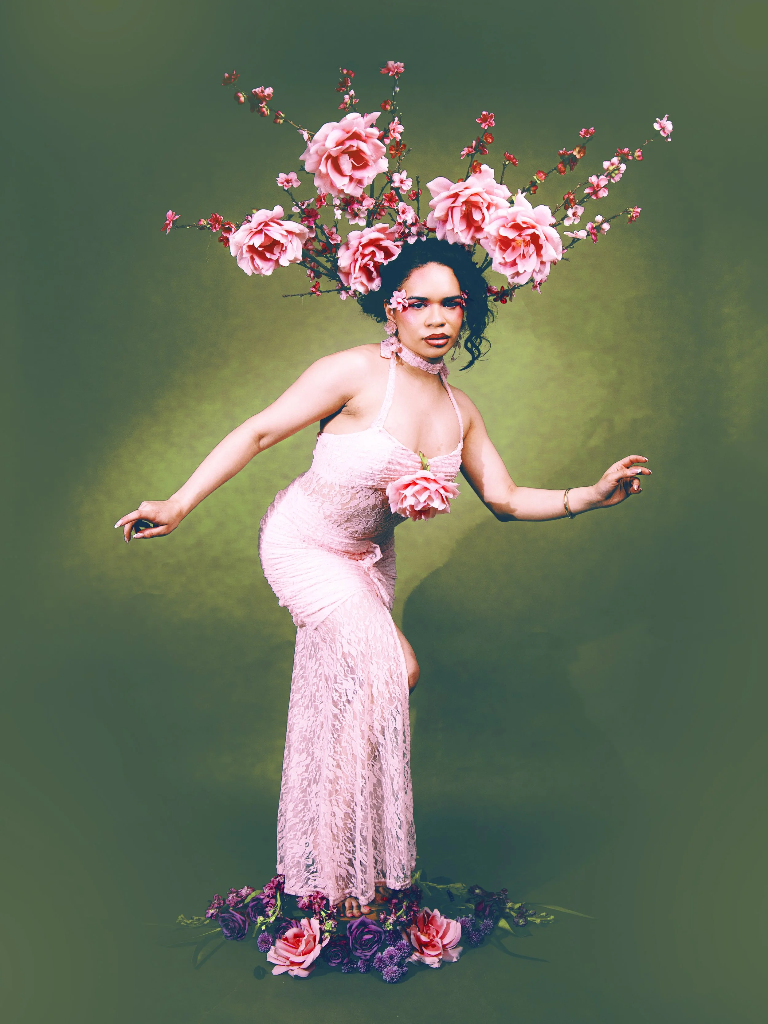 Local Dallas, Texas, DFW Non-traditional Editorial Creative Portraits Cover Art Photographer. @roseypears .A woman with dark curly hair wearing a pink lace dress and floral accessories, standing on a floral arrangement, with large pink flowers and a 