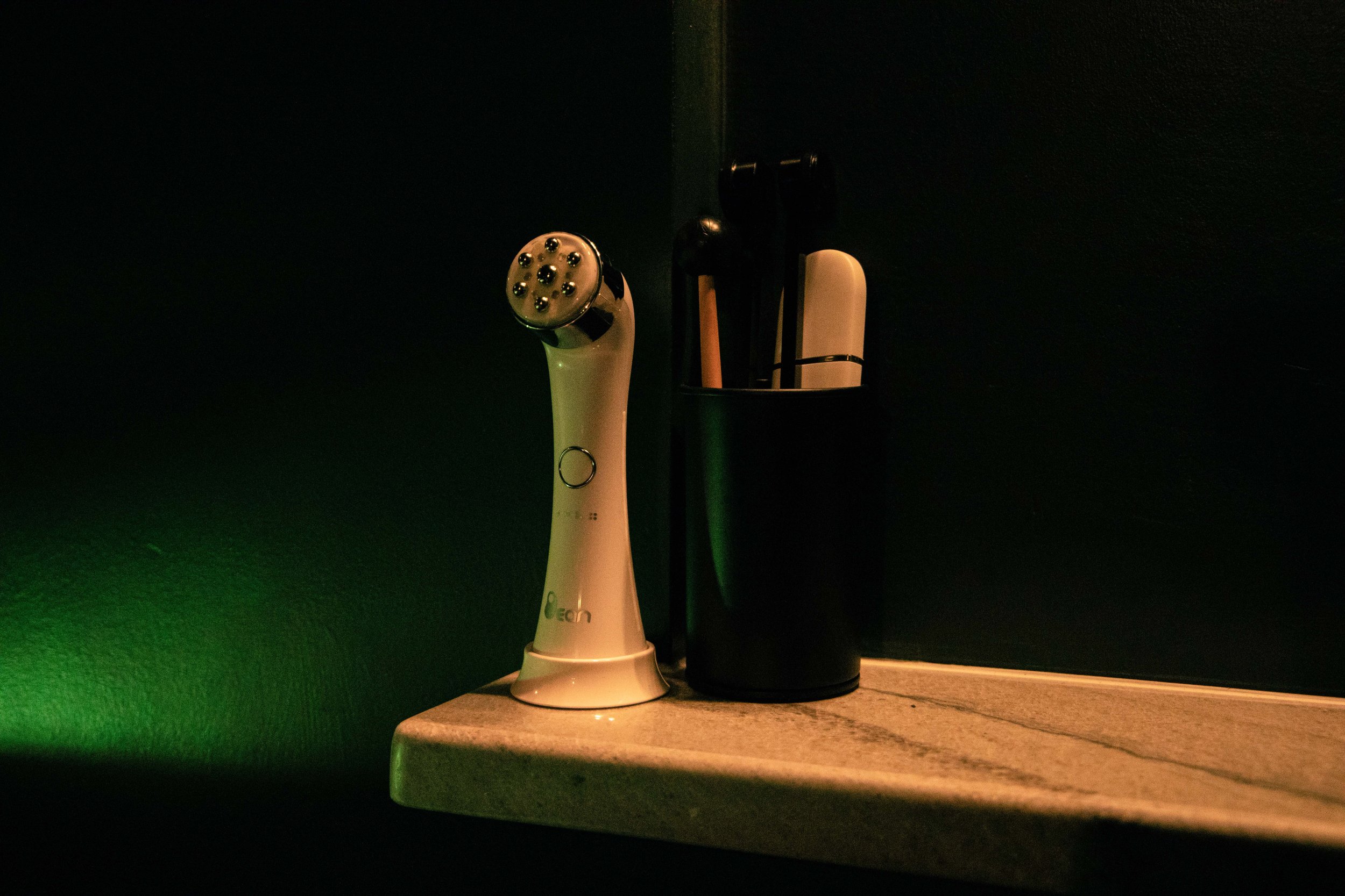 An electric toothbrush and a black cup on a wooden surface with dark background.
