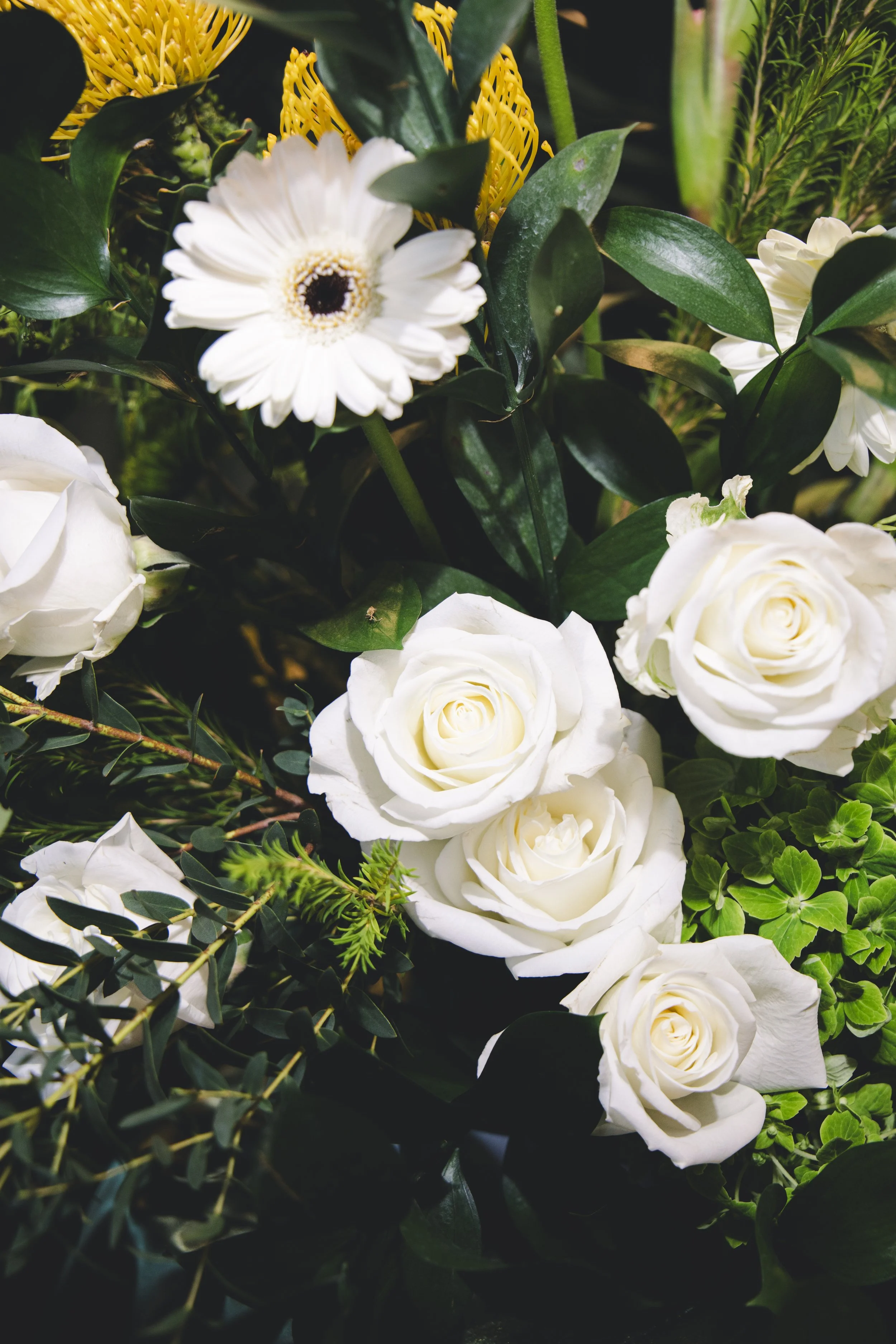 Arrangement of white roses, a white gerbera daisy, green leaves, and yellow decorative elements.