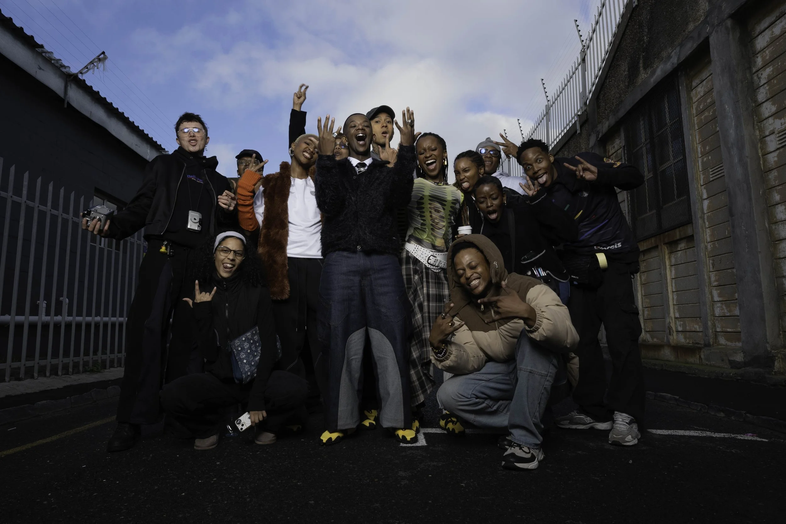 Group of diverse happy people posing together outdoors in an urban setting, some making peace signs, one person holding a camera, dressed in casual and colorful clothing, celebrating and expressing joy. Puma Campaign with Maglera