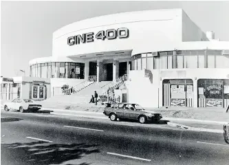 A vintage movie theater called CINE 400 with a rounded Art Deco design, steps leading up to the entrance, and classic cars parked in front, likely from the mid-20th century. Historic Cape Town Movie Theatres. Culture during the time of Apartheid.