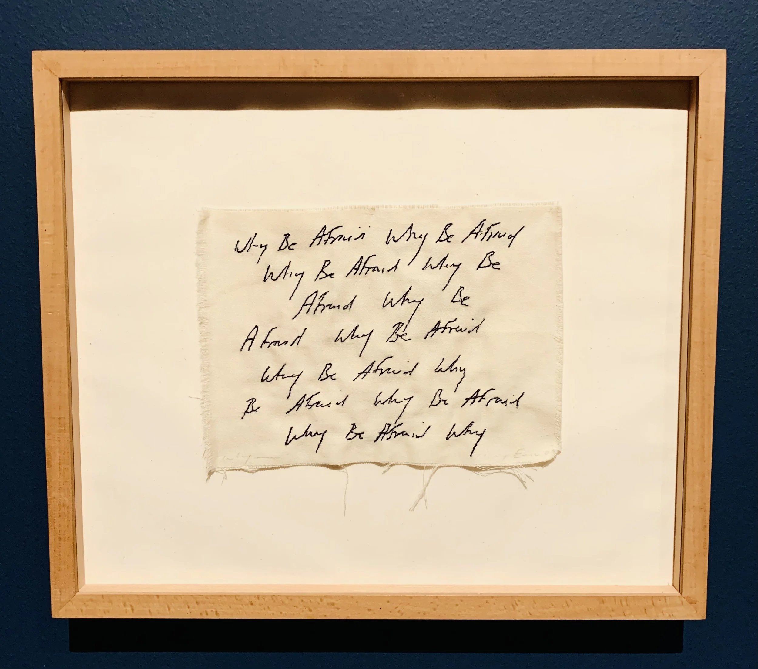The words why be afraid embroidered on to white textile by Tracey Emin and mounted inside a wooden frame.