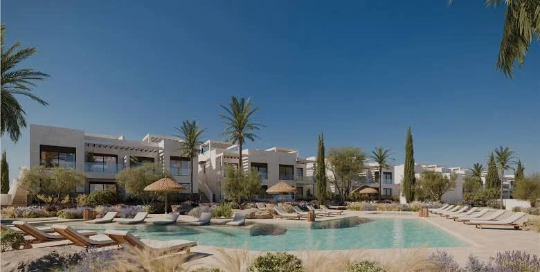 Luxury resort pool area with lounge chairs, palm trees, and modern buildings in the background under a clear blue sky.