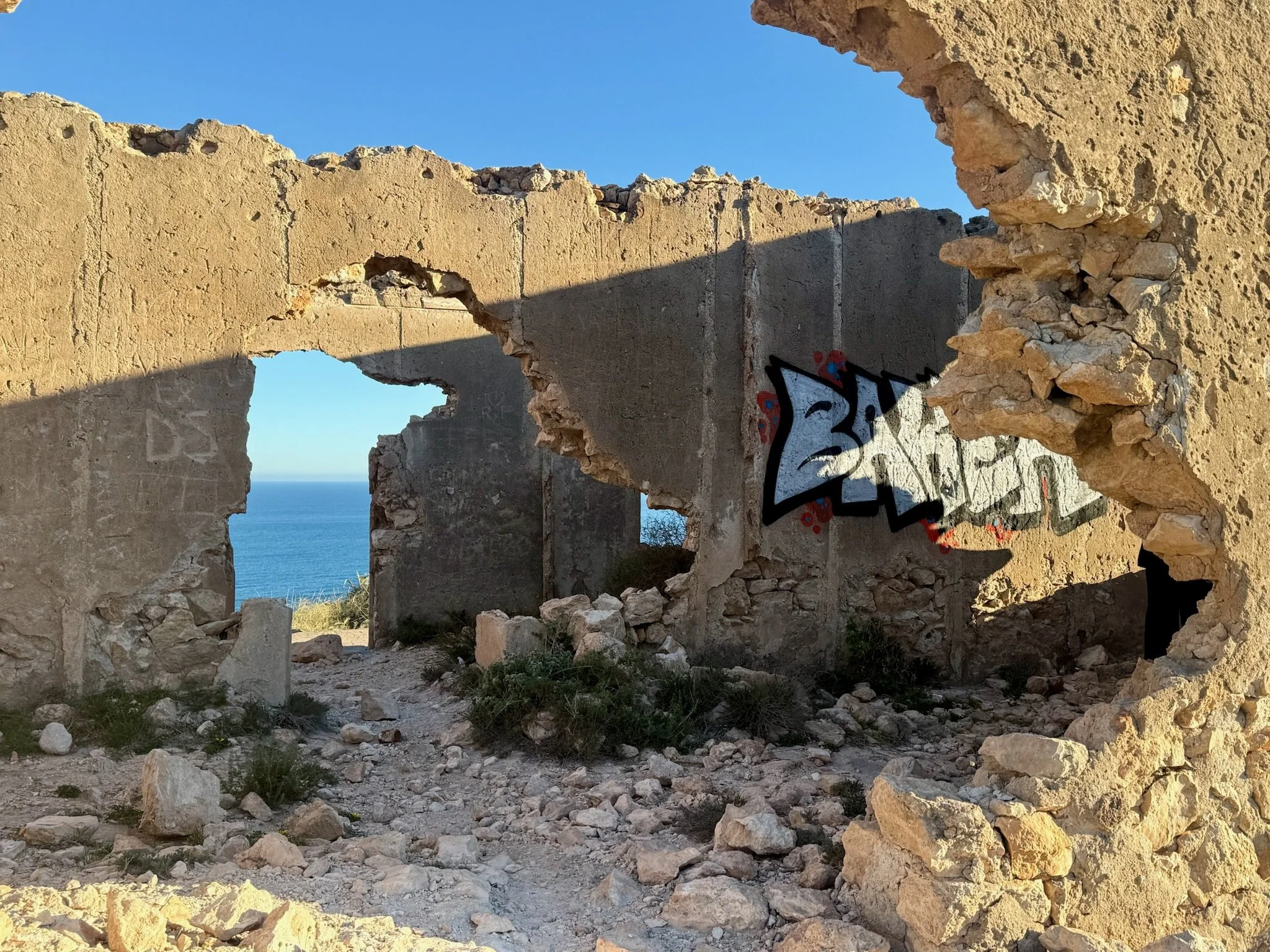 Ruins of an old stone building with a large opening, revealing a view of the ocean and blue sky in the background.