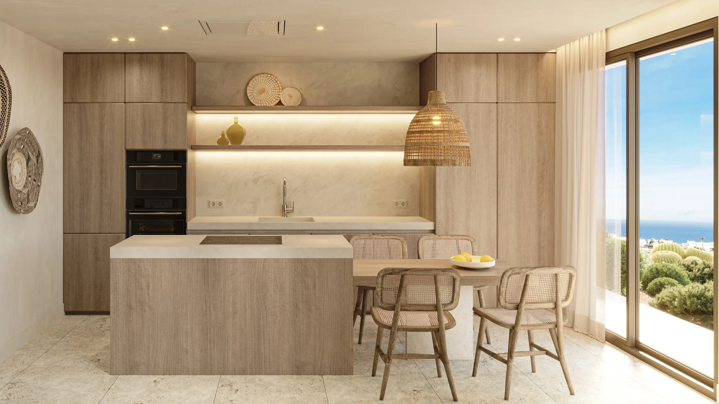 Modern kitchen with beige cabinetry, a white marble countertop, and a built-in oven. There is a hanging woven pendant light, decorative baskets and jars, and a large window with a view of the outdoors, including the ocean and greenery.