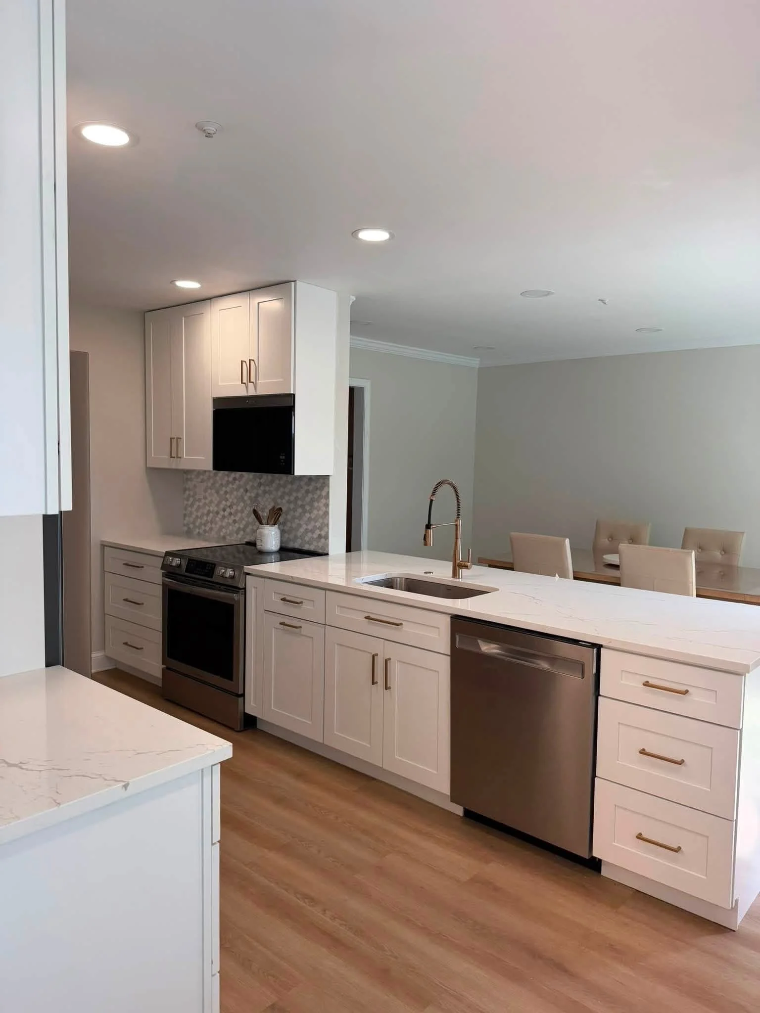 Modern kitchen with white cabinets, stainless steel appliances, marble countertop, and wooden flooring.