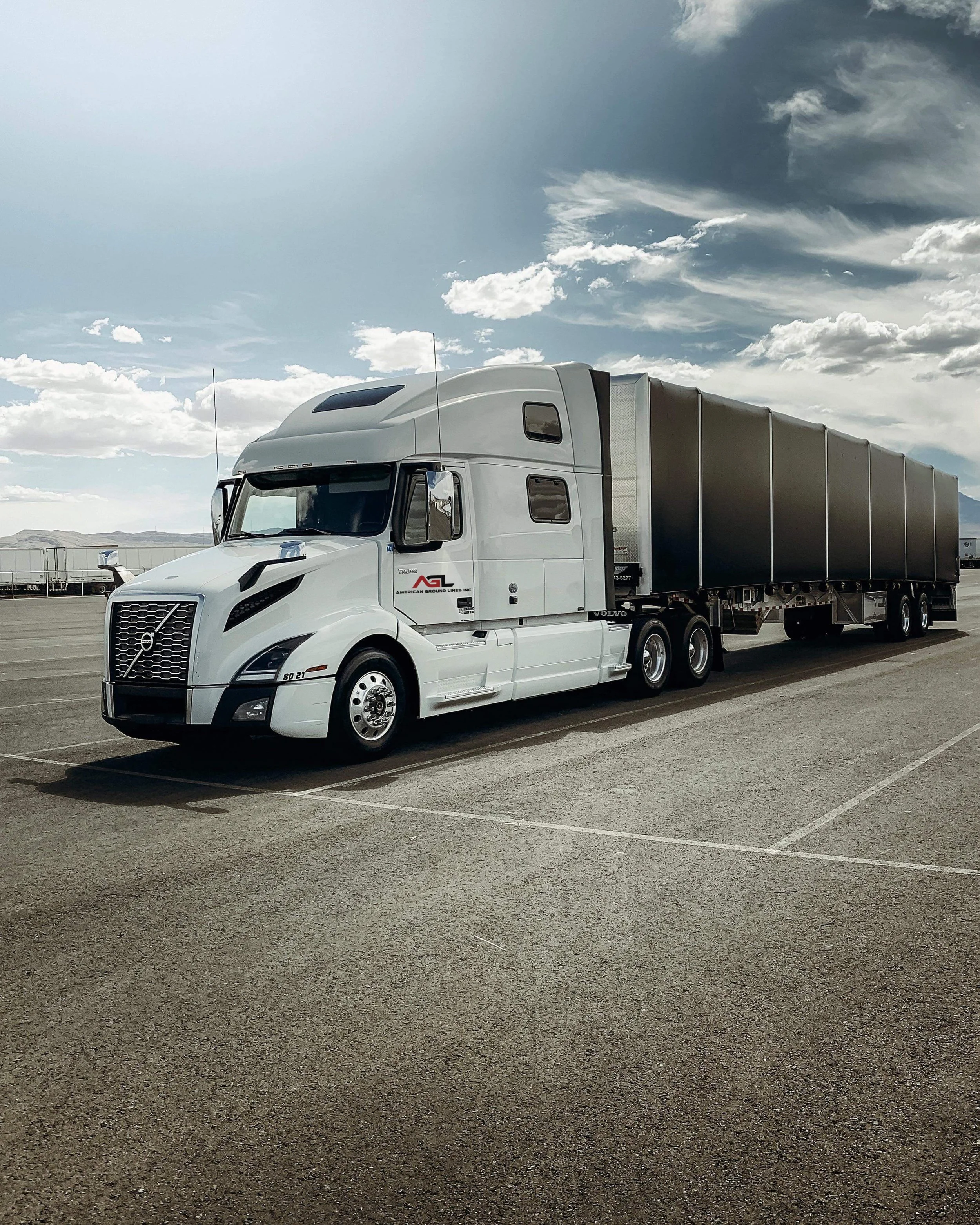 White semi-truck with a trailer parked in an open parking lot under a partly cloudy sky.
