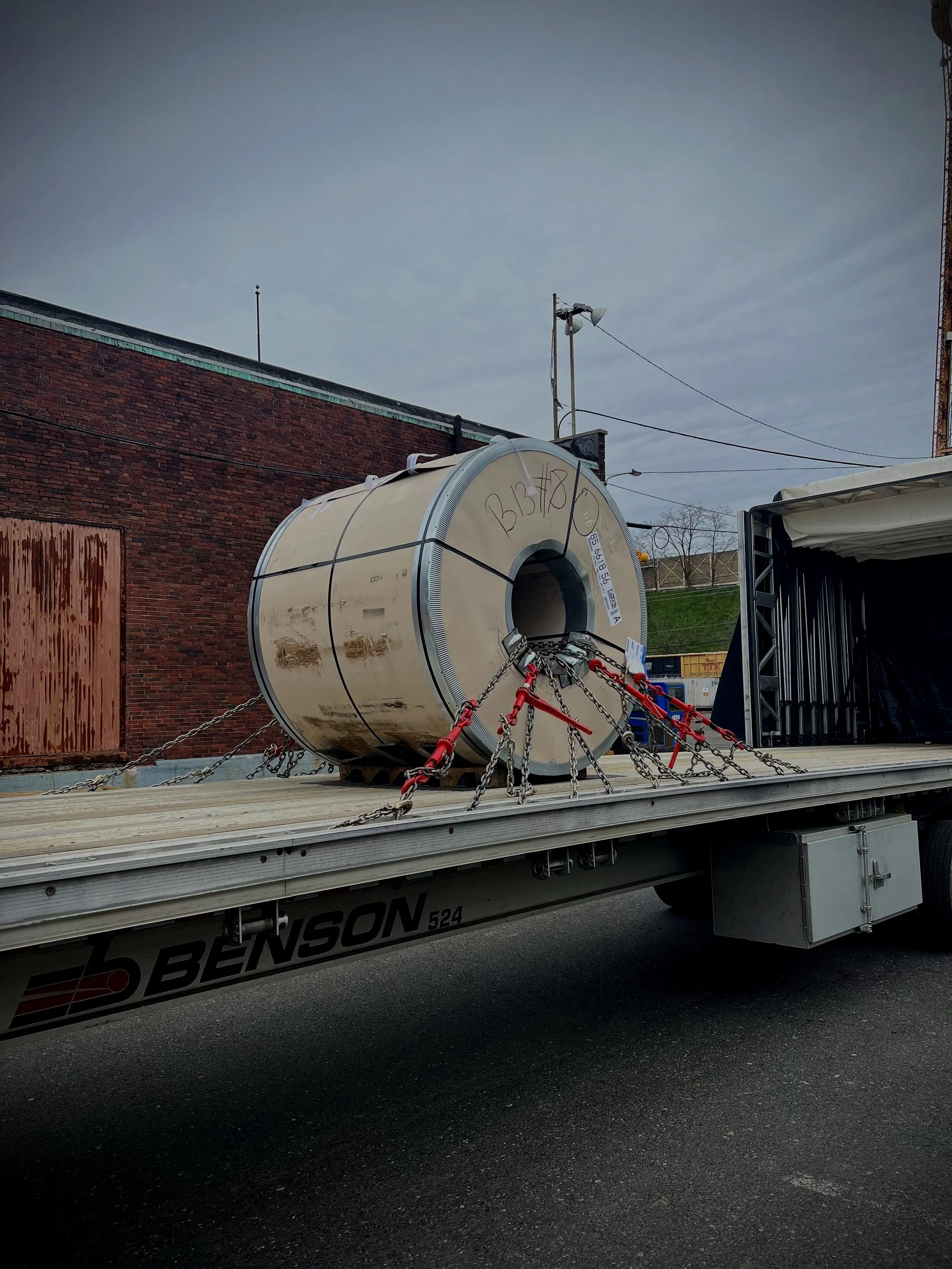 American Ground Lines flatbed transporting a 48,000-lb steel coil secured with chains.