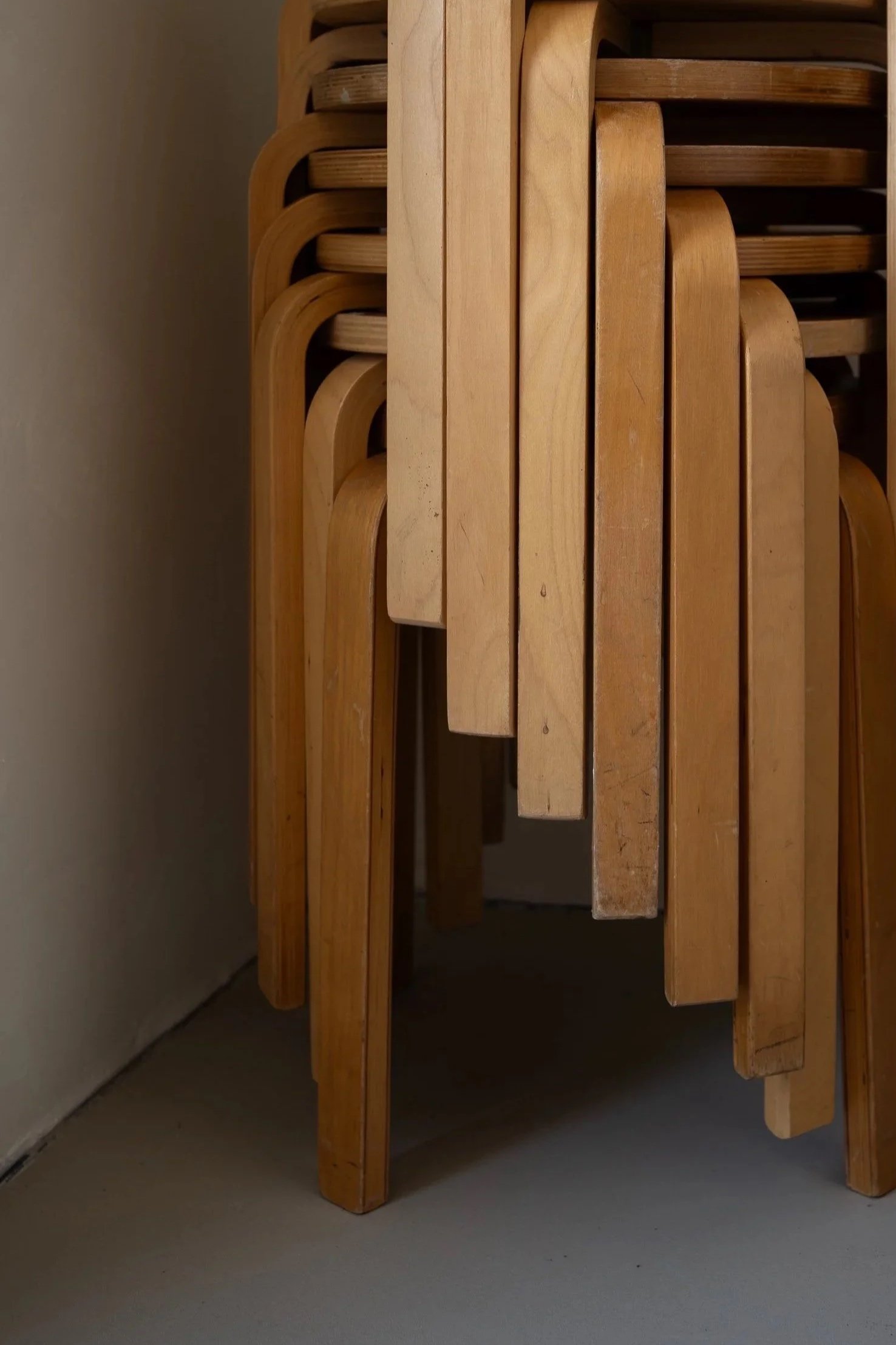Een stapel houten stoelen tegen een muur, waarvan sommige op hun kant liggen.