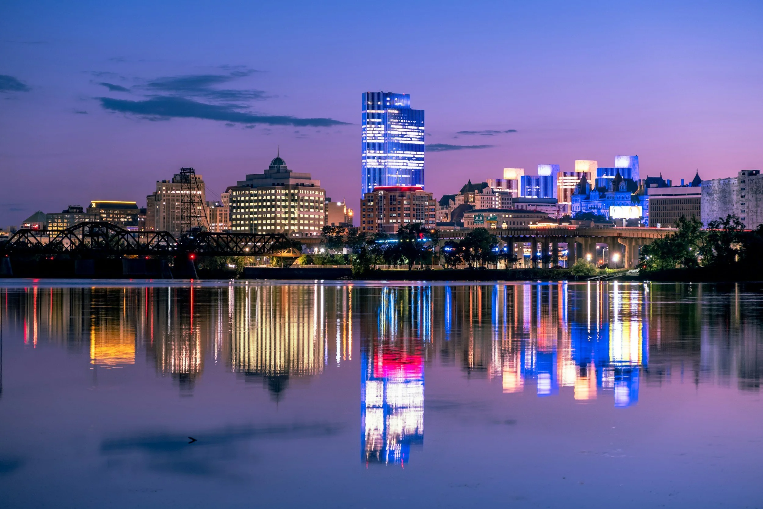 Night city skyline with illuminated buildings and their reflections on the water.