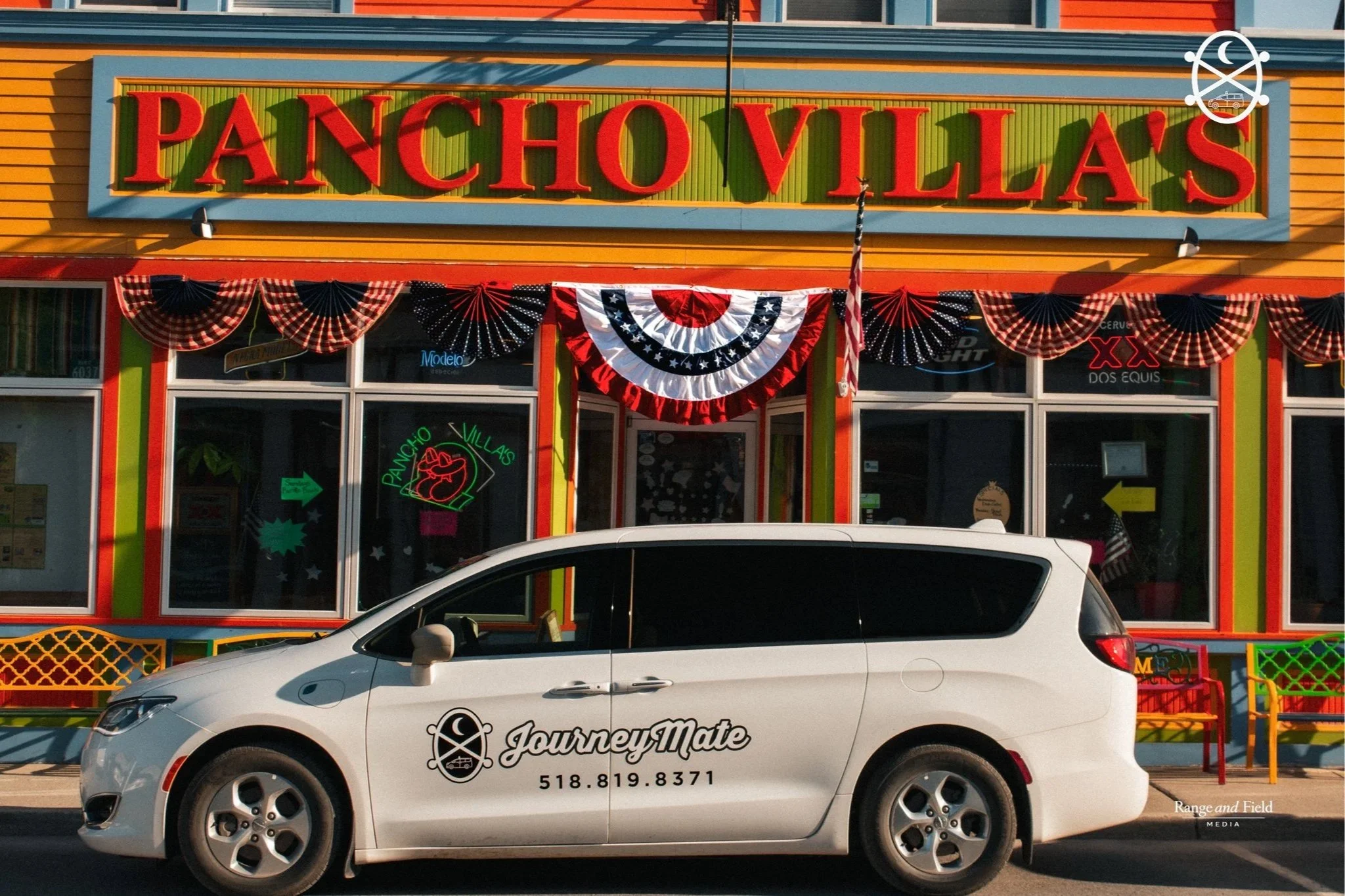 Colorful building with a sign that reads "PANCHOVILLAS" in large red letters, decorated with patriotic bunting and American flags, with a white car parked in front with company branding and contact information.