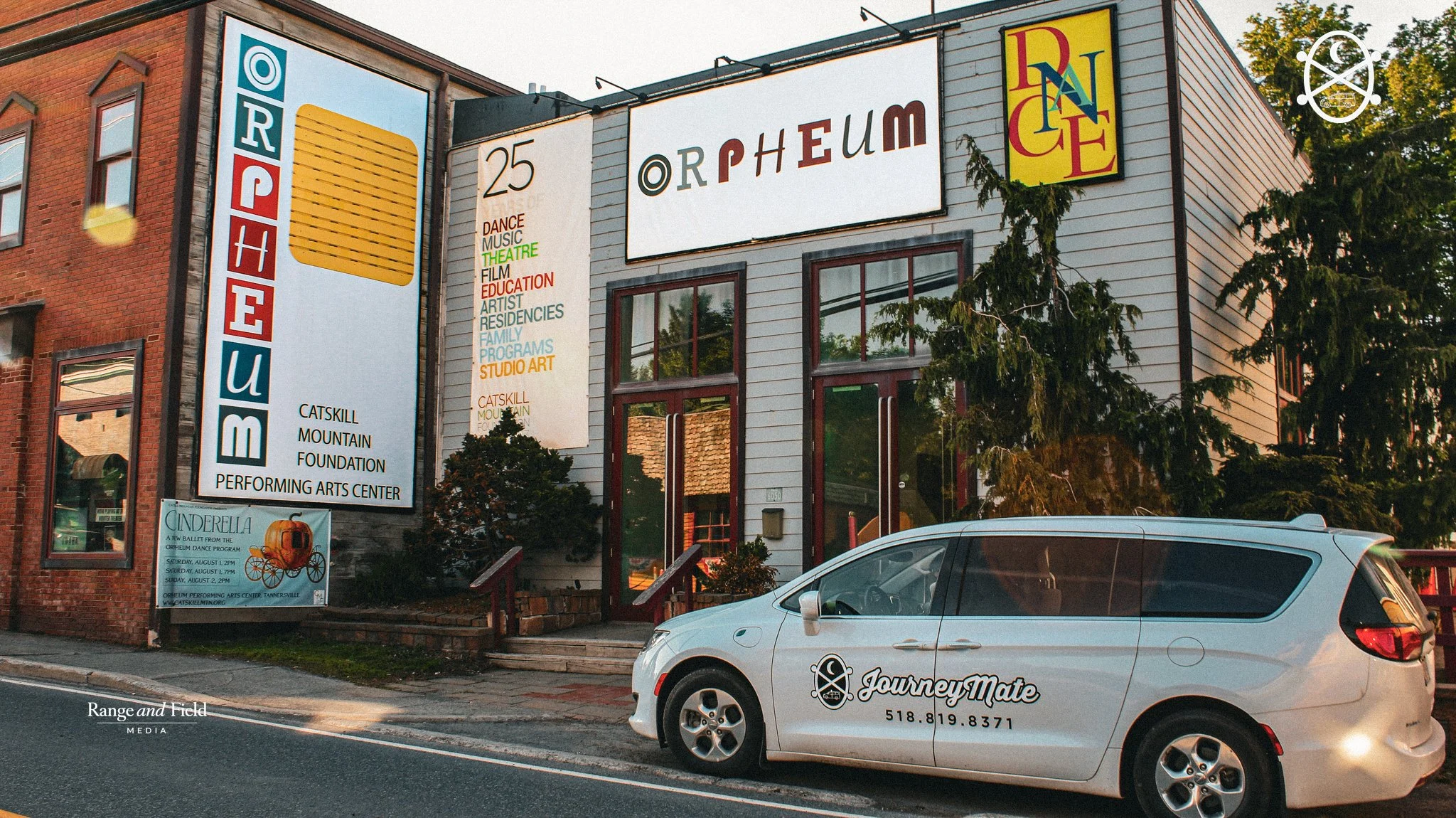 The Orpheum Performing Arts Center building with signs advertising dance, music, theater, film, education, artist residencies, family programs, studio art, and a Catskill Mountain Foundation. There is a white JourneyMate vehicle parked in front.
